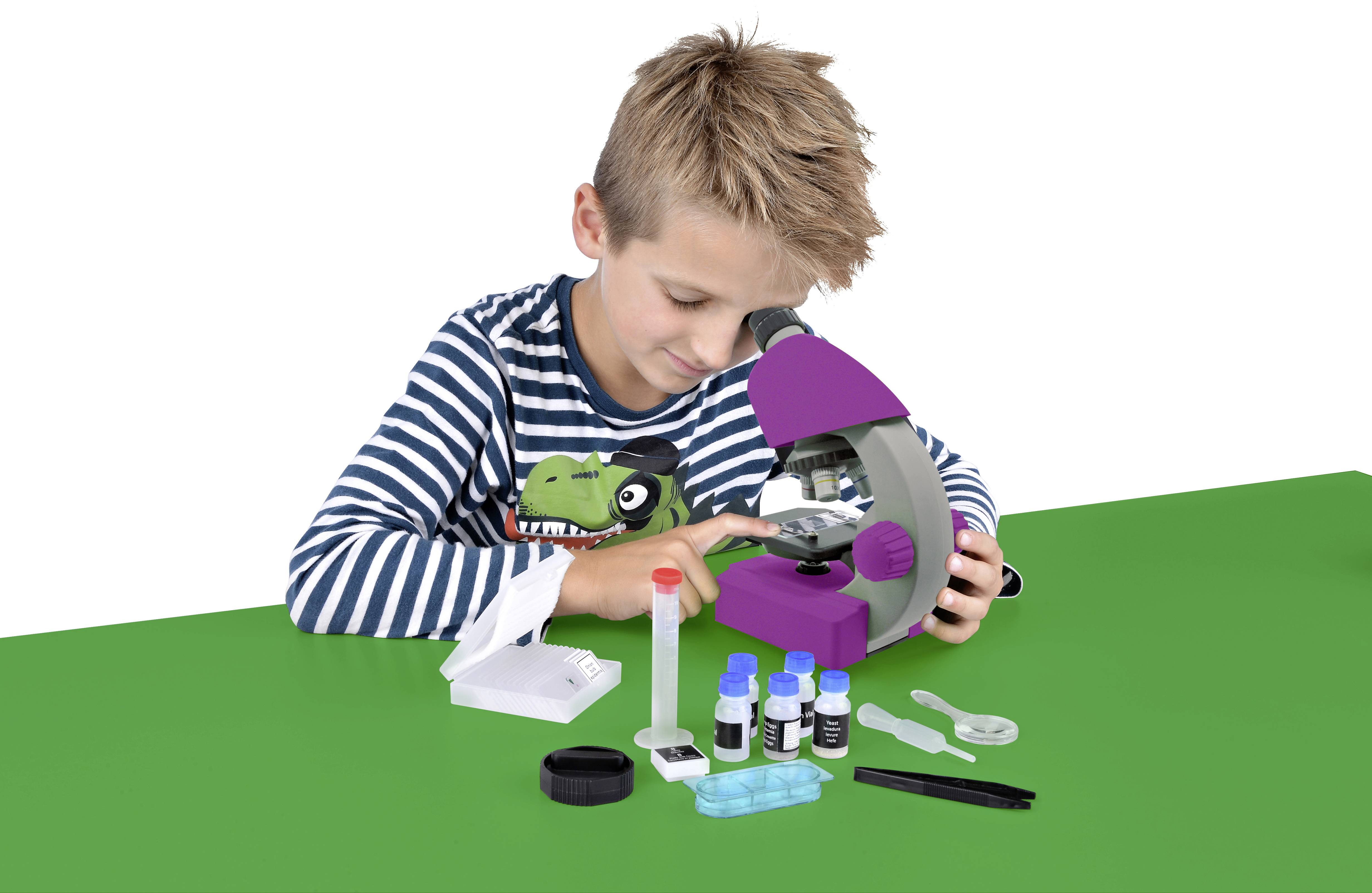 Een kind onderzoekt iets met een microscoop, omringd door laboratoriumbenodigdheden op een groene tafel.