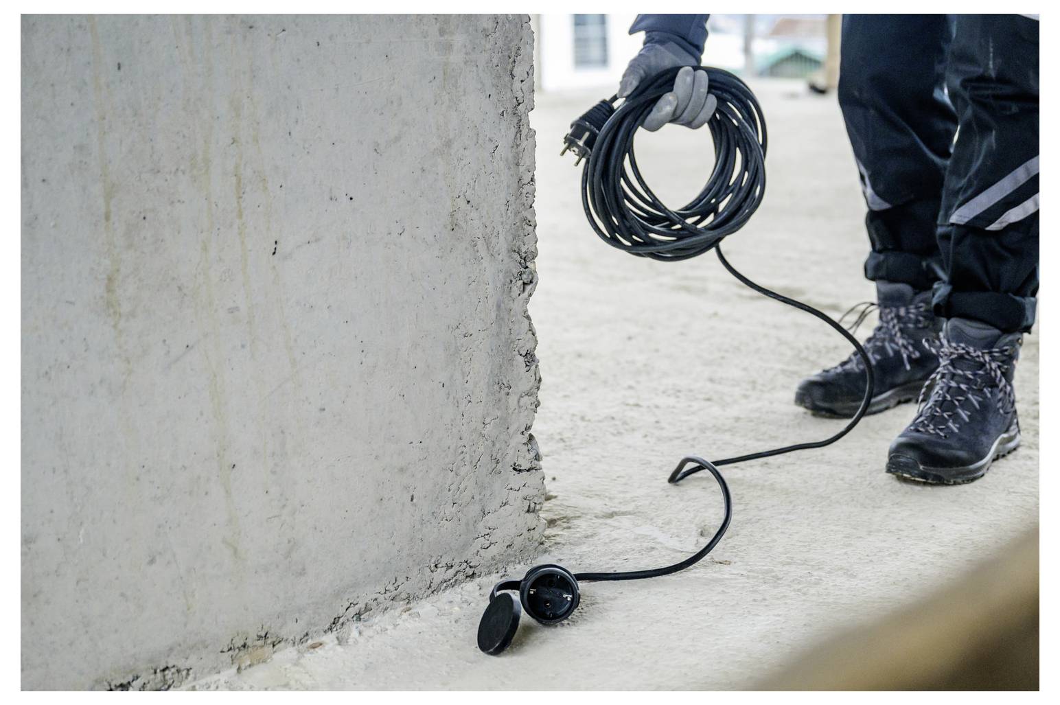 Werknemer met opgerold kabel naast een beschadigde betonnen muur, met een headset en snoer op de grond