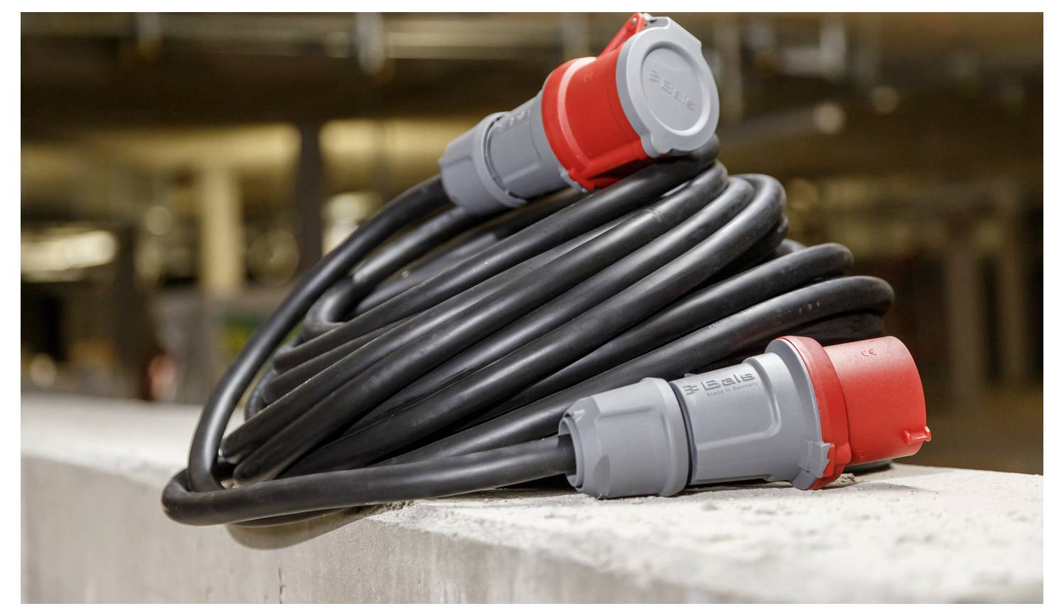 Opgerold zwaar elektrisch kabel met rode en grijze industriële stekkers rustend op een betonnen richel.