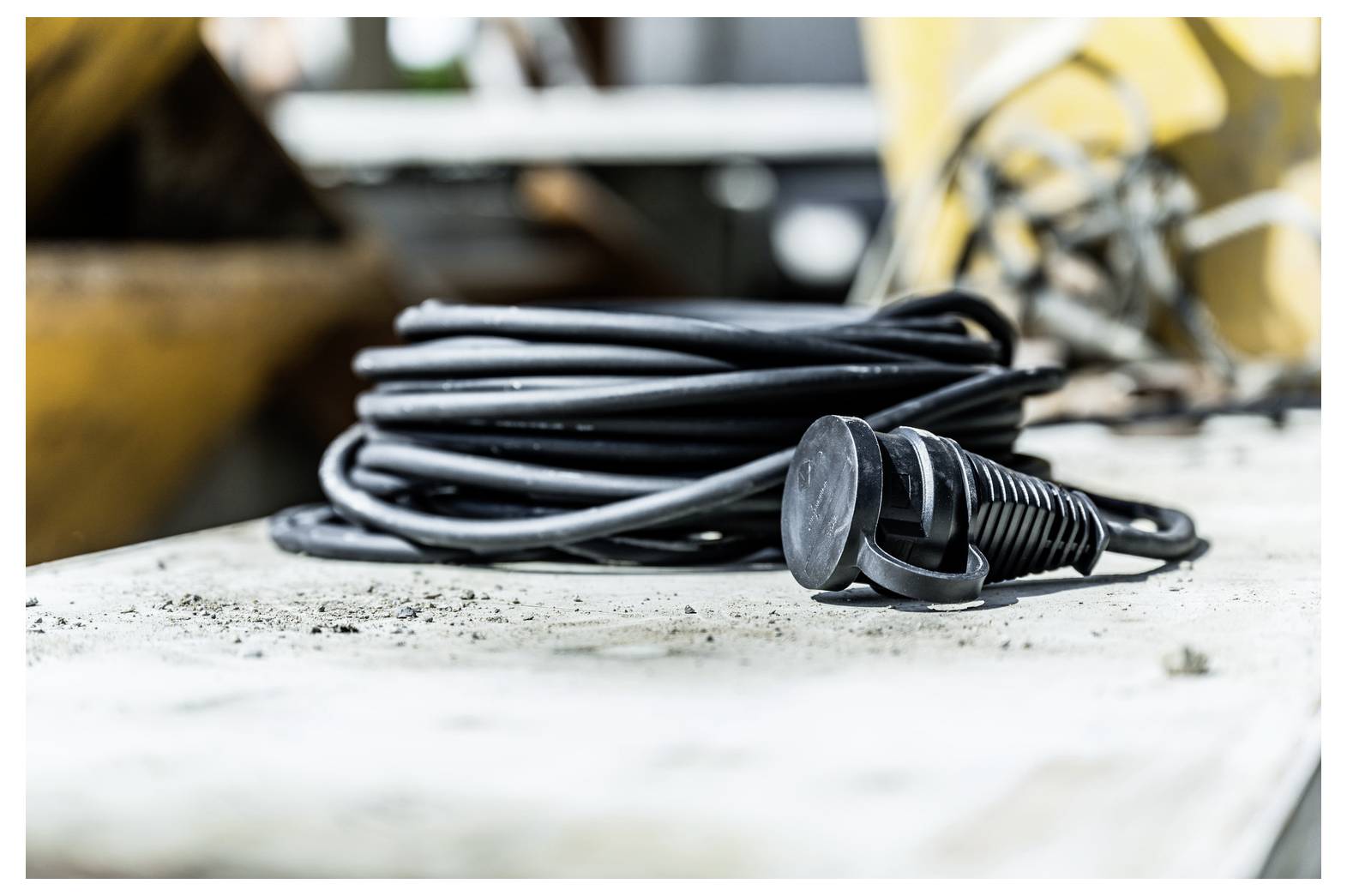 Opgerold zwart elektrisch stroomnoer met stekker liggend op een stoffige werkbank in een werkplaats.