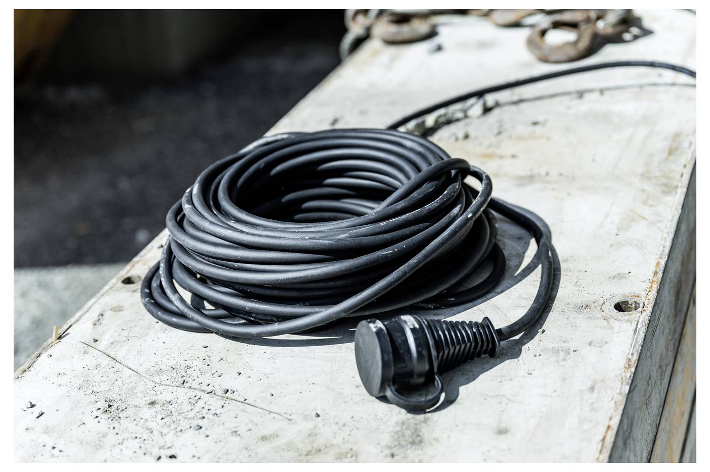 Opgerold zwart snoer met een connector rustend op een versleten wit werkoppervlak.