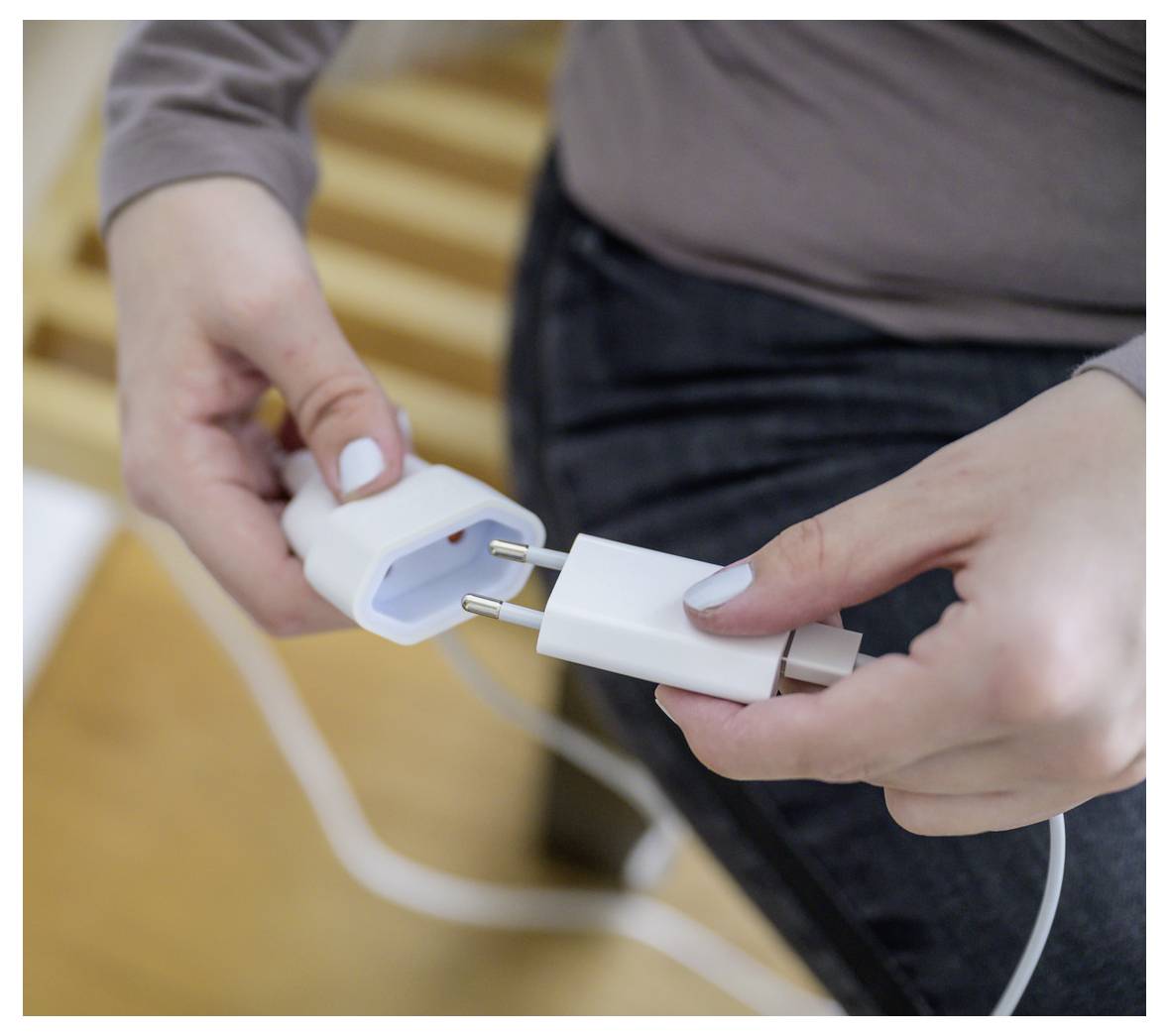 Handen die een stekker en adapter verbinden, waarop iemand zich voorbereidt om een elektrisch snoer binnenshuis in te pluggen.