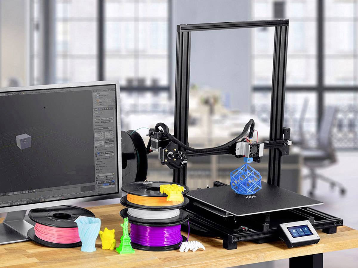 Een 3D-printer op een bureau drukt een blauw rooster van kubussen af. Naast de printer staan filamentrollen in verschillende kleuren. Op het beeldscherm draait een 3D-modelleringsprogramma.