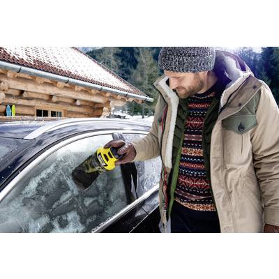 Een man in winterkleding krabt met een gele ijskrabber ijs van de autoruit. Op de achtergrond ziet men een houten hut in de sneeuw.