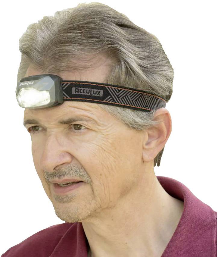 Een man draagt een hoofdlamp met een verlichtend licht, draagt een rood poloshirt en heeft grijs haar.