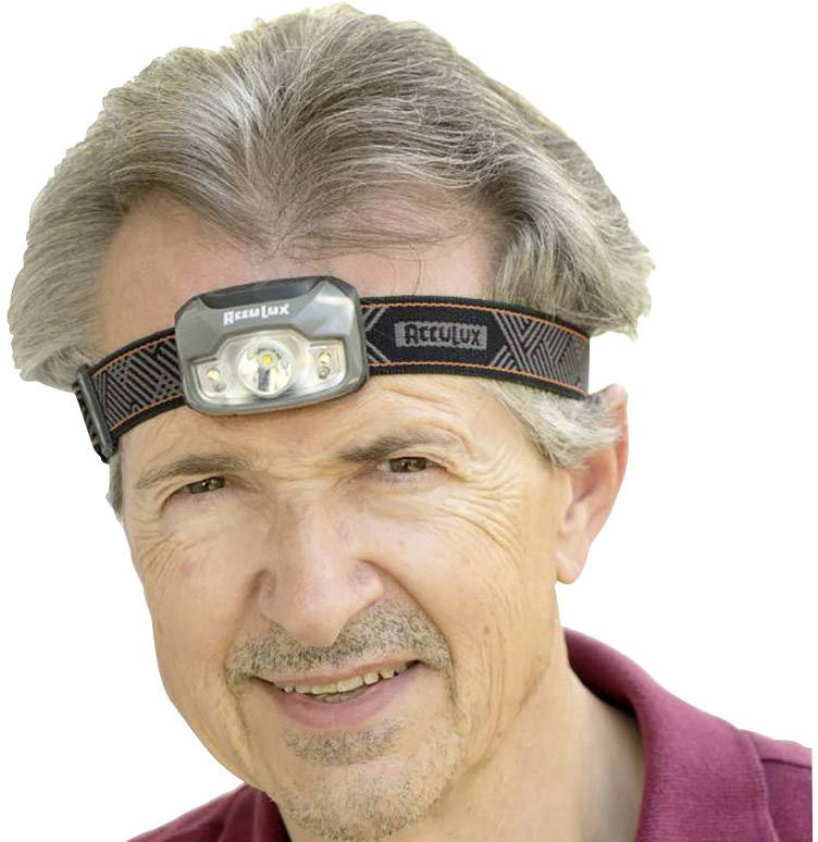 Een persoon draagt een hoofdlamp en glimlacht. De hoofdlamp is van het merk AccuLux. De persoon draagt een rode bovenkant.