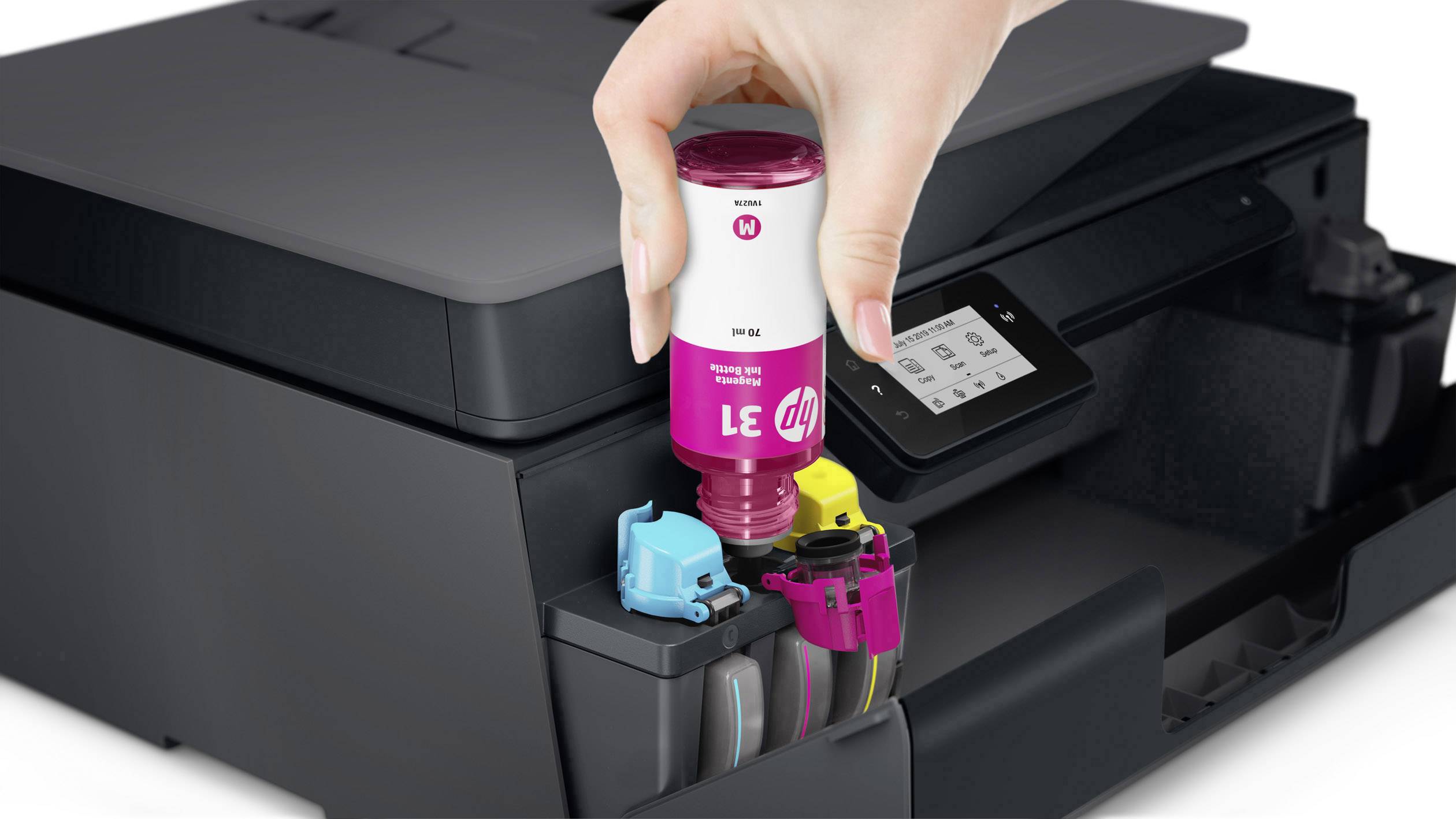 Een hand vult magenta inkt in een printerlnktank, naast de gele en blauwe tank. De printer heeft een display.