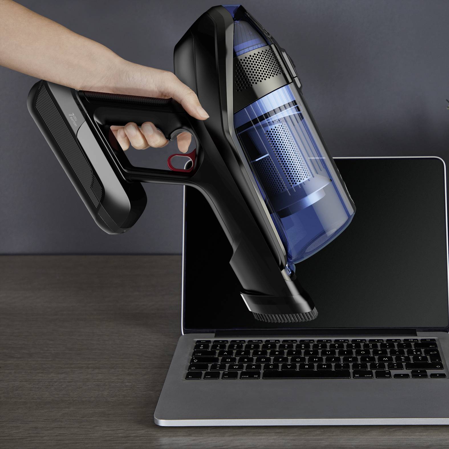 Een hand houdt een stofzuiger boven een laptoptoetsenbord om vuil te verwijderen.