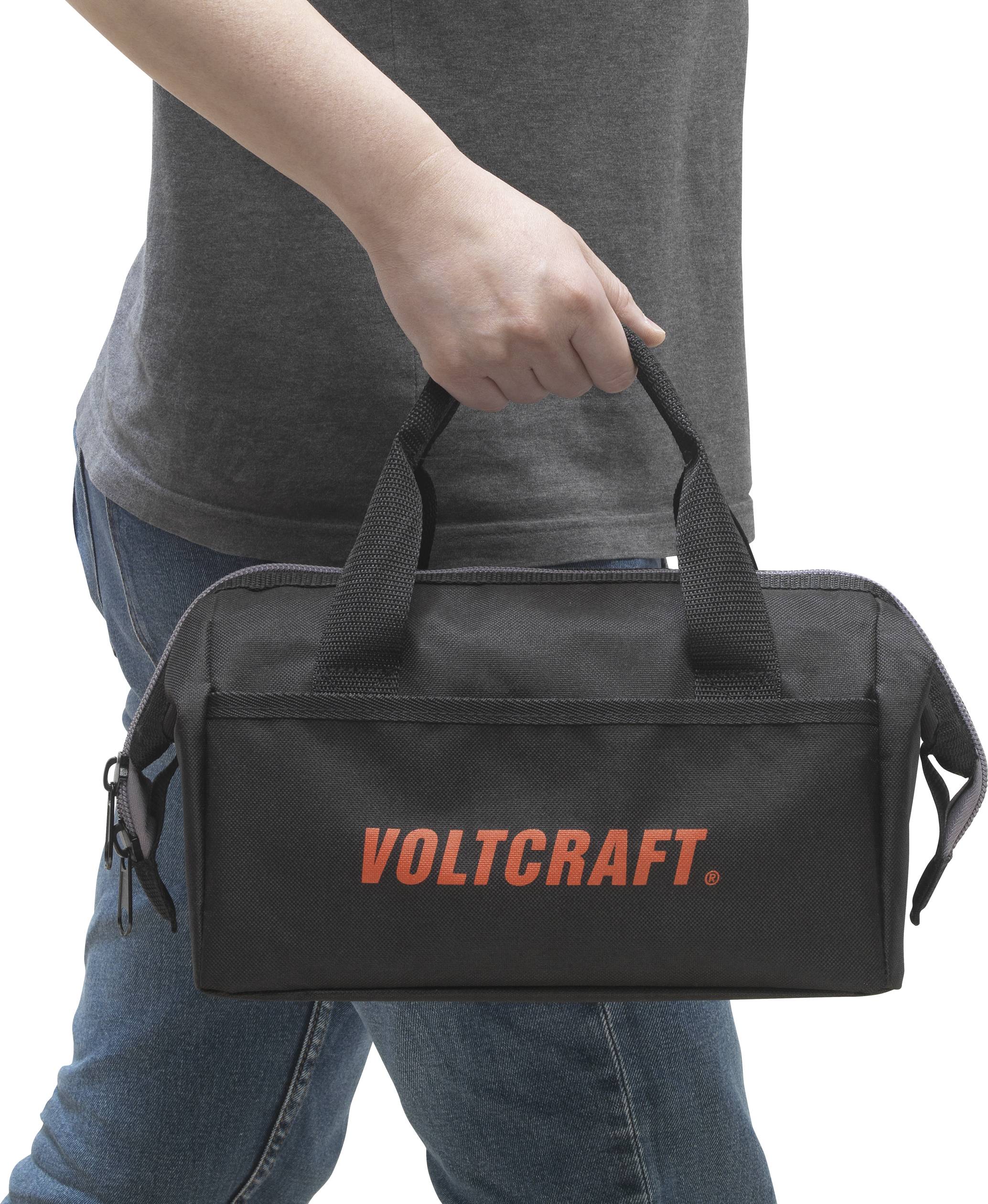 Een persoon houdt een zwarte Voltcraft-gereedschapstas met rits en draaggrepen.