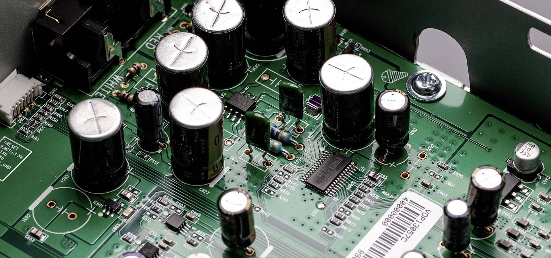 Een close-up van een groene printplaat met verschillende elektronische componenten, waaronder meerdere condensatoren en chips.