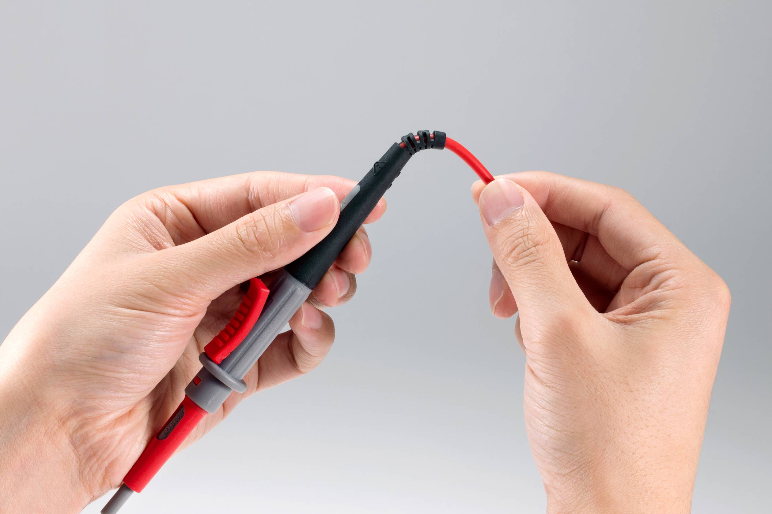 Een persoon houdt een rood kabel vast met twee handen, waarbij één hand het uiteinde met een stekker omklemt.