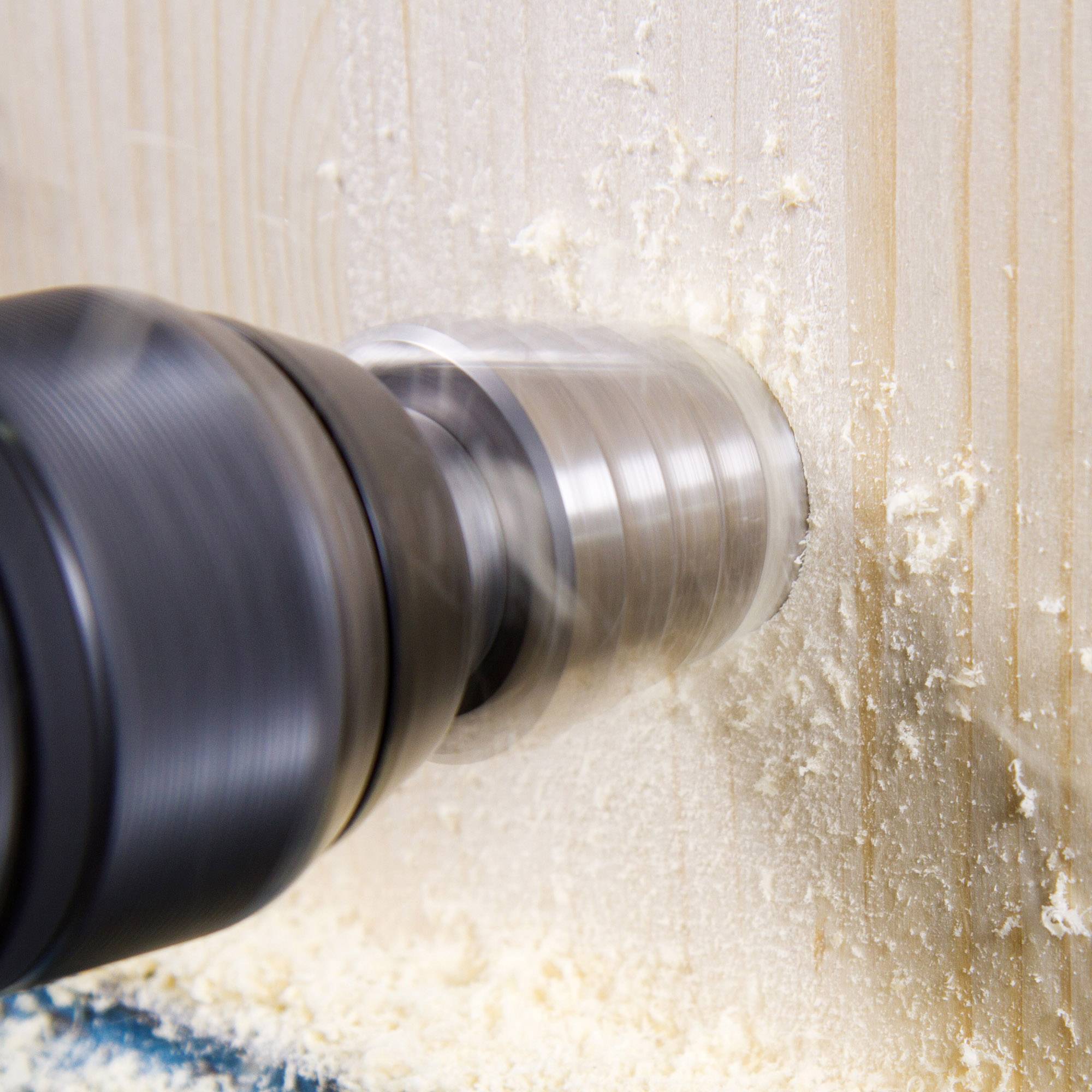 Een boormachine boort een rond gat in een houten plank. Houtspaanders vliegen rond.