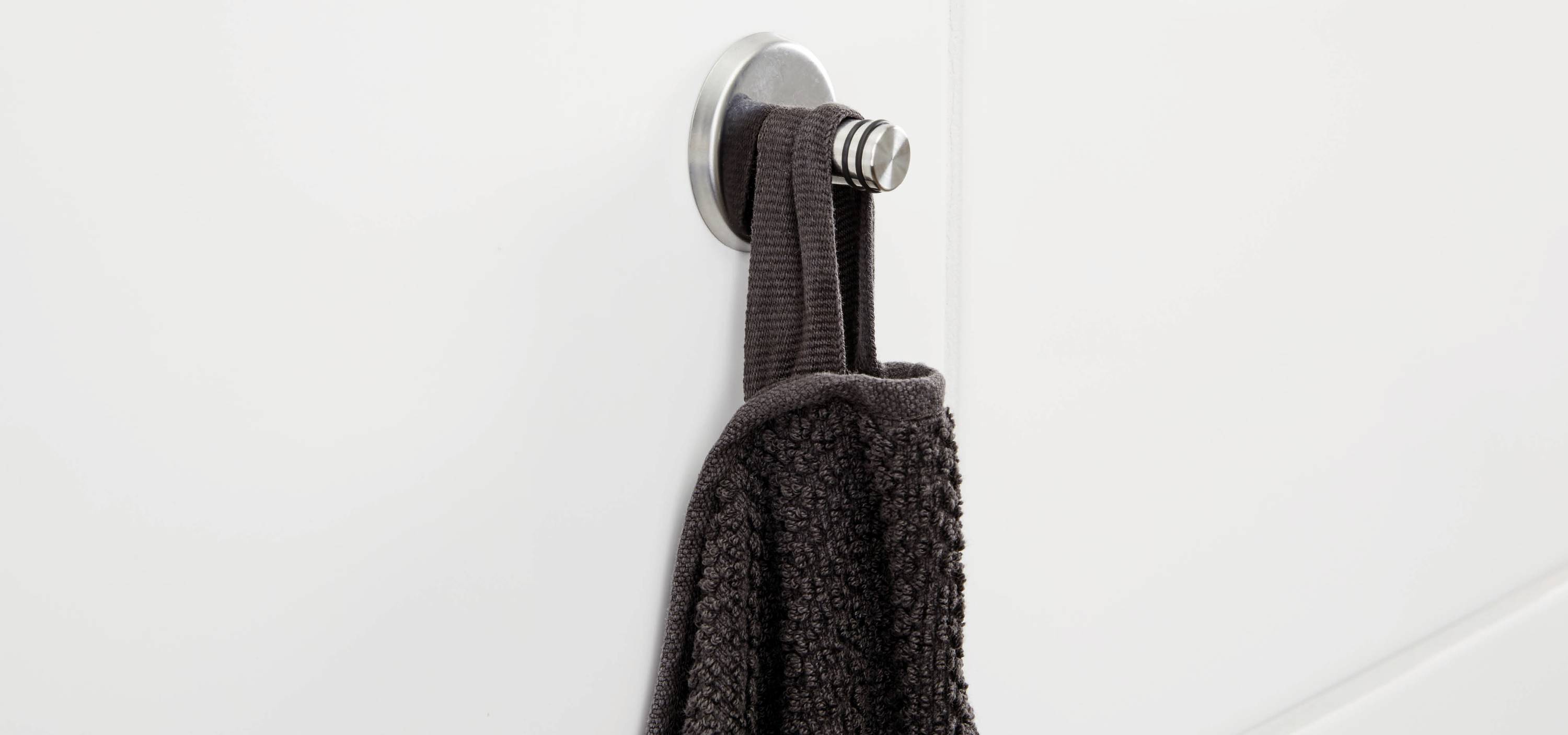Een donkerbruin handdoek hangt aan een moderne, zilveren haak aan een witte muur.