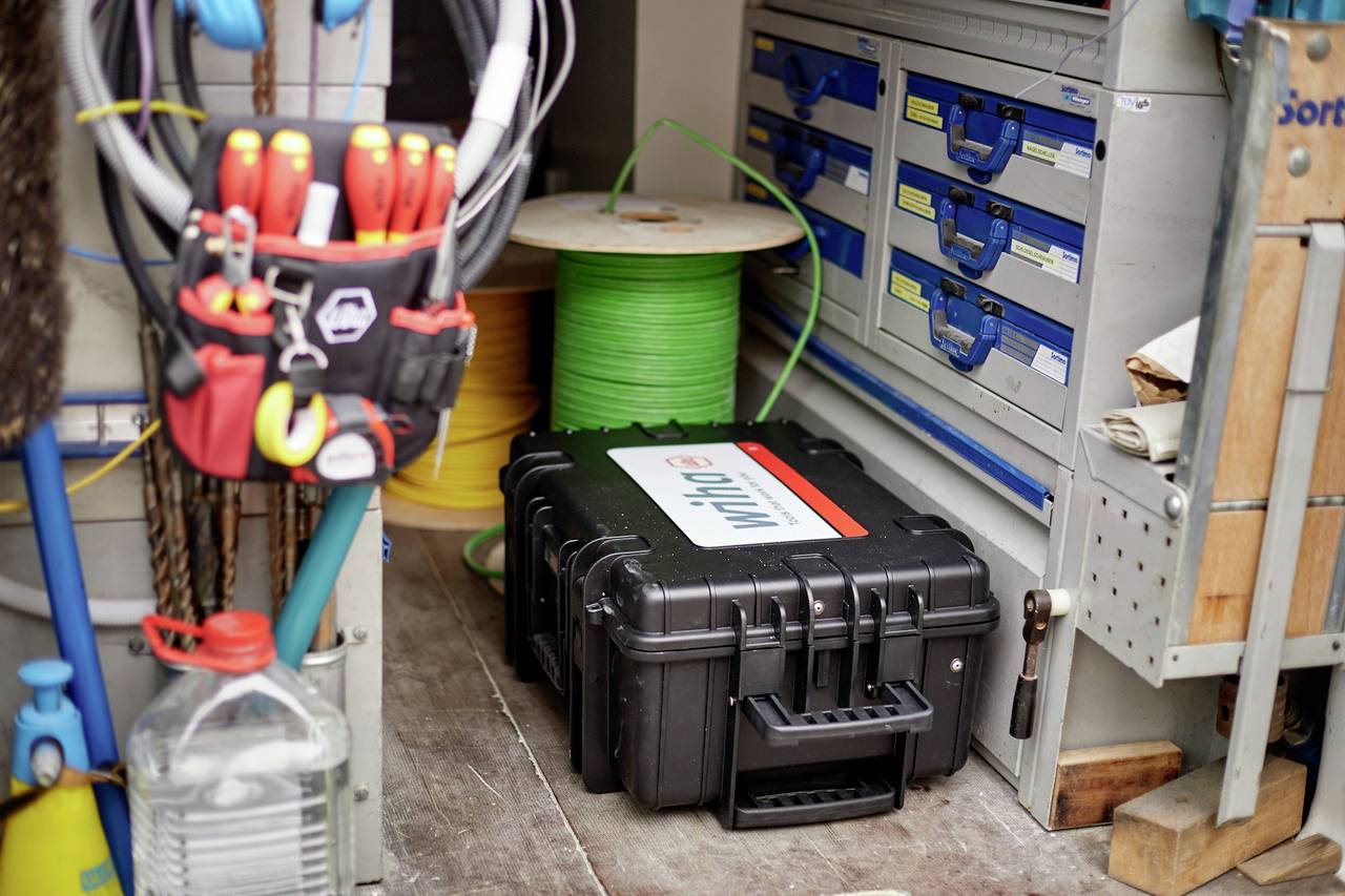 'Gereedschapskisten en kabelhaspel in een gereedschapswagen. Rondom liggen gereedschappen en apparaten, netjes gerangschikt in rekken en tassen.'