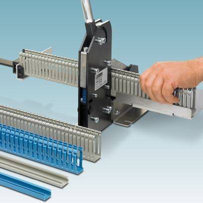Een gereedschap scheidt kunststof kabelgoten op een blauwe ondergrond. Een hand houdt het werkstuk vast.