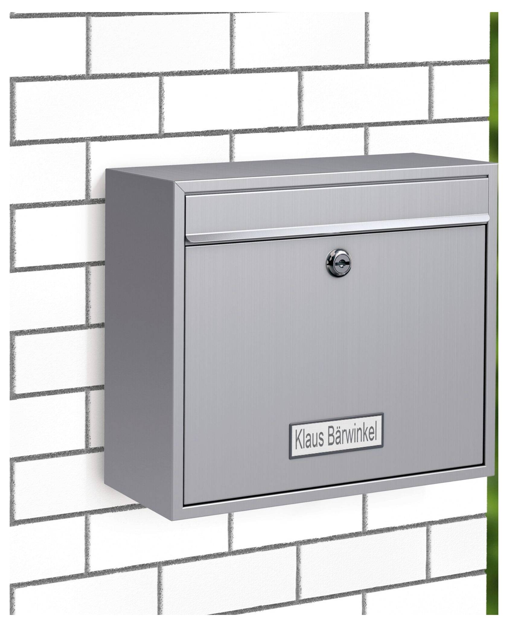 Een grijze brievenbus met een slot is bevestigd aan een witte bakstenen muur. Een naamplaatje leest 'Klaus Bärwinkel'.