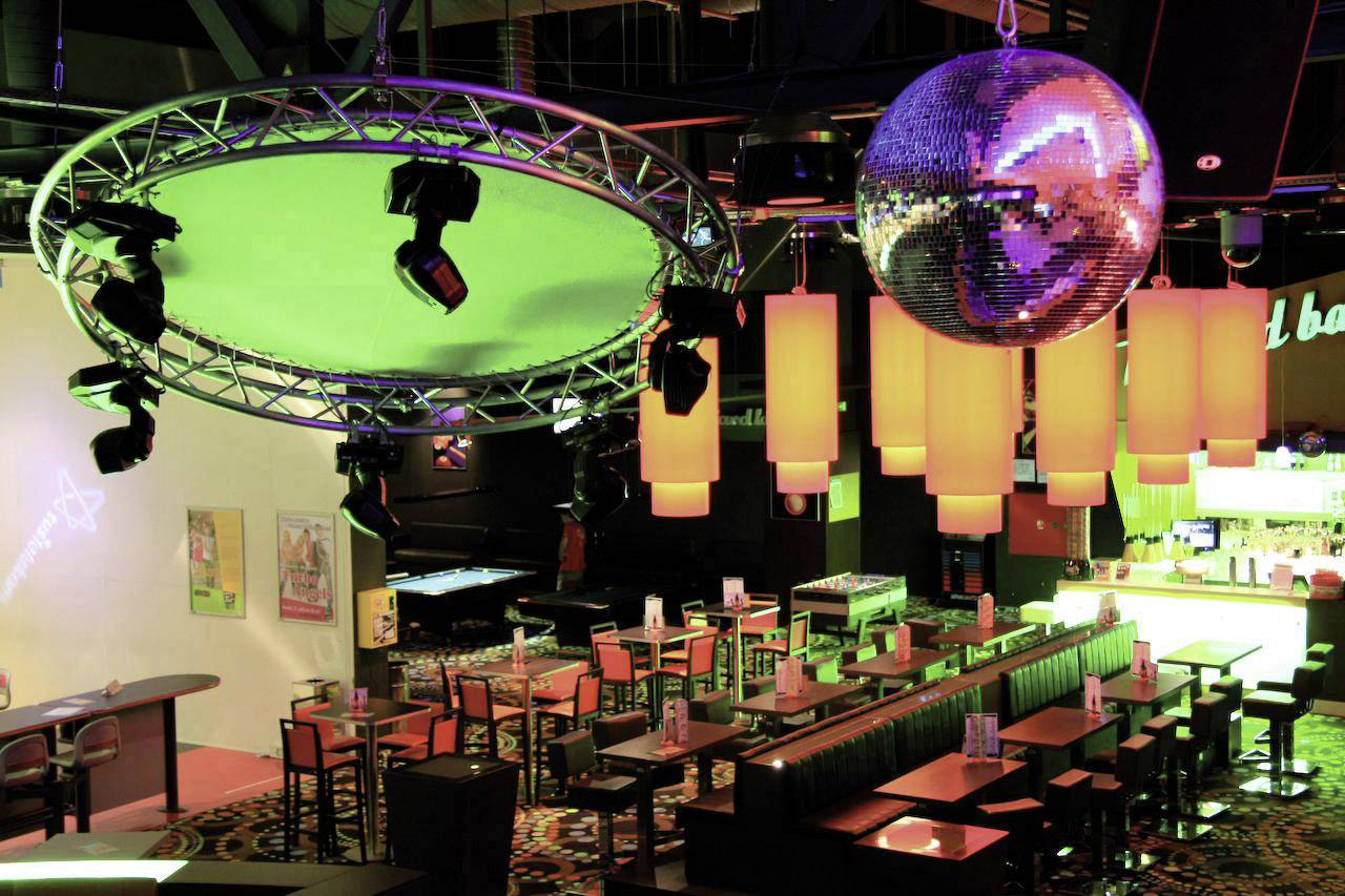 Een kleurrijke feestruimte met tafels, een bar en een grote discobal aan het plafond die veelkleurige lichten weerkaatst.