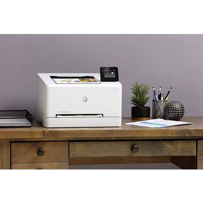 Witte printer op een houten tafel, naast planten, schrijfwaren en papier, tegen een paarse muur.