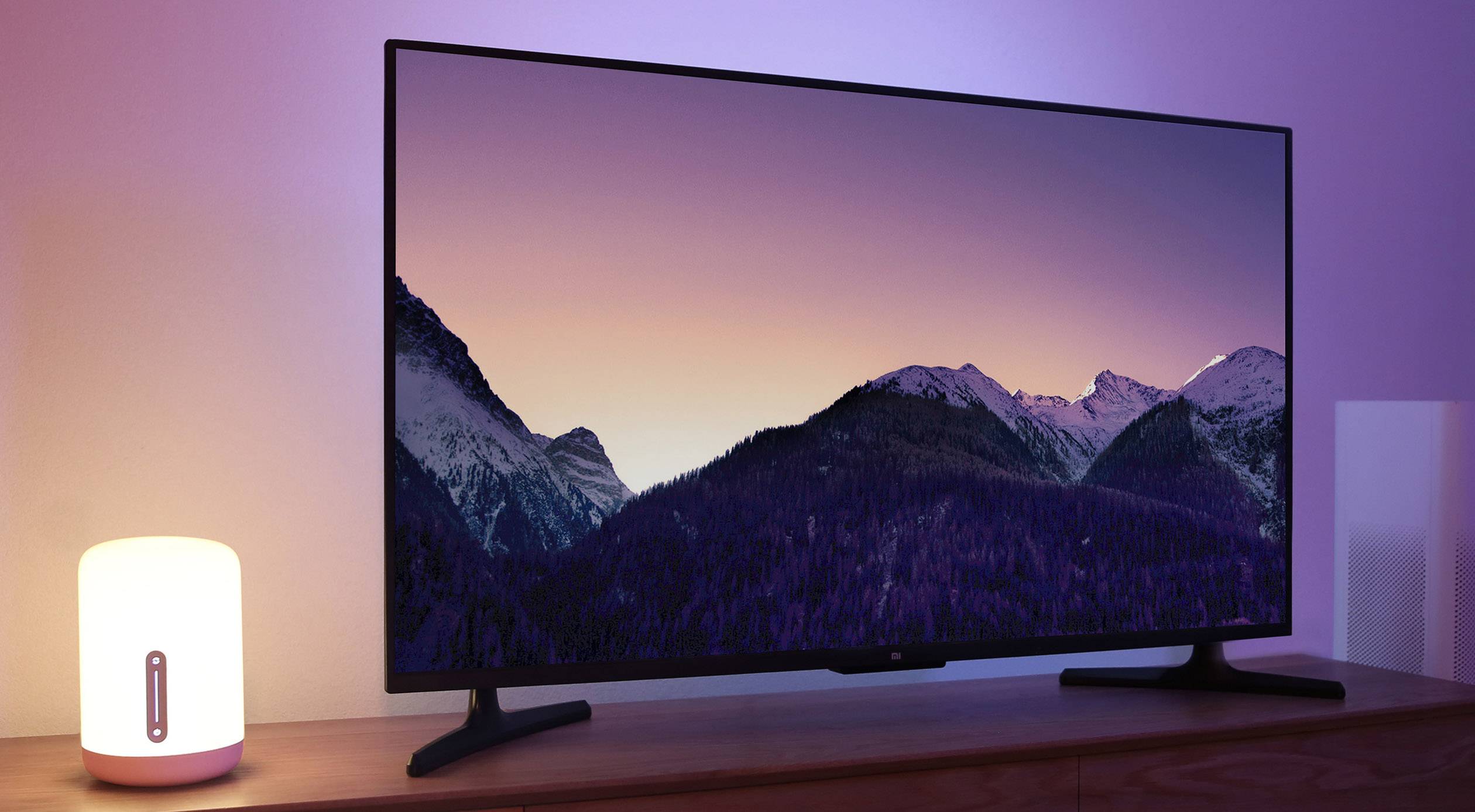 Een tv-scherm toont een landschapsfoto met besneeuwde bergen bij zonsondergang. Ernaast staat een aangestoken tafellamp.