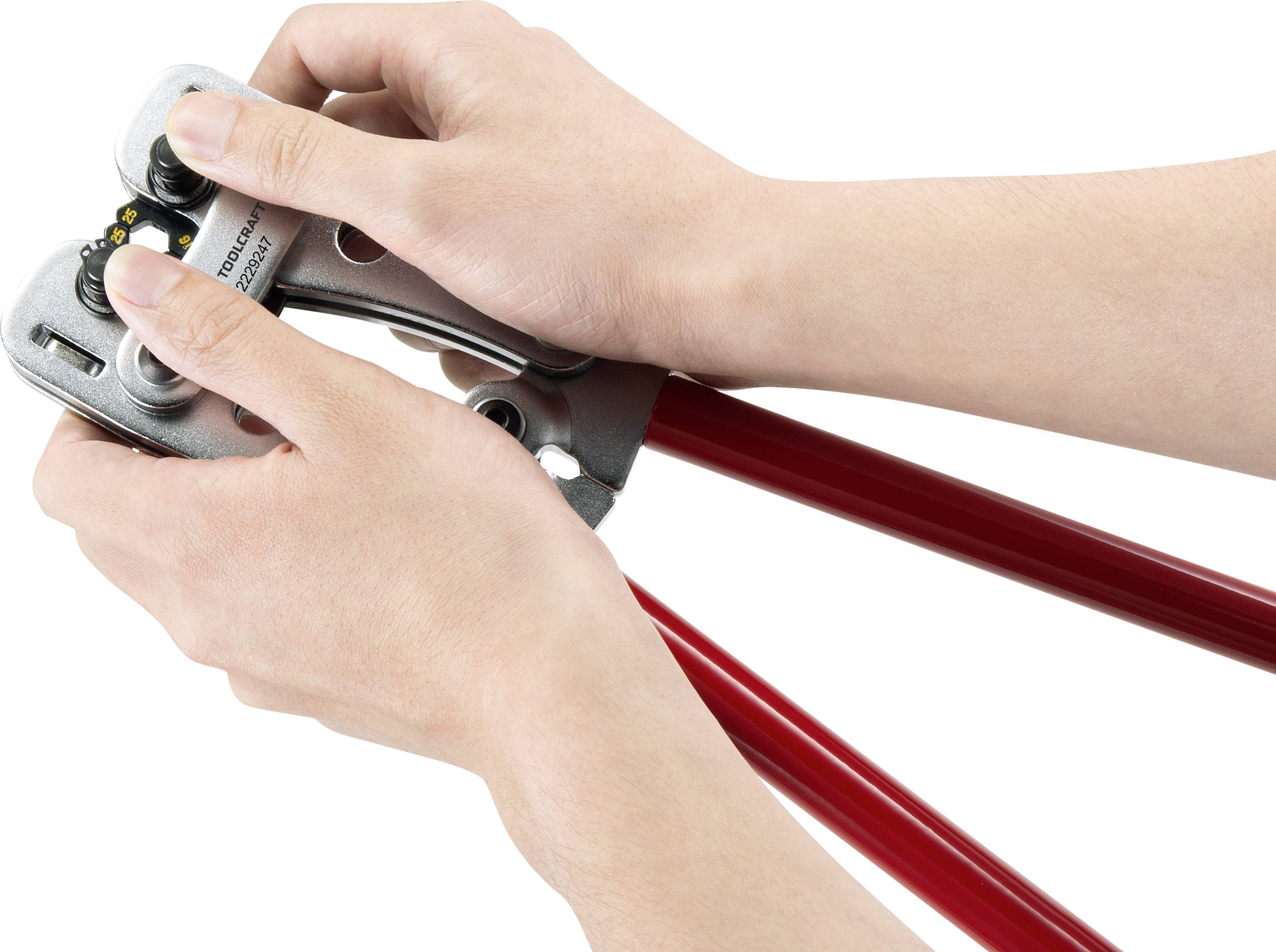 Een persoon gebruikt een boutenschaar om een dik metalen kabel door te knippen. De snijkop en rode handvatten zijn zichtbaar.