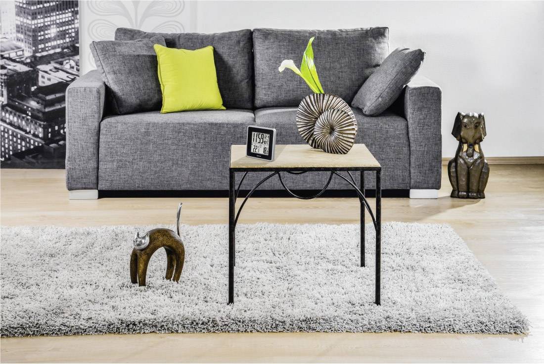 Grijze bank met geel kussen, houten tafel met decoraties en abstracte sculptuur op tapijt in moderne woonkamer.