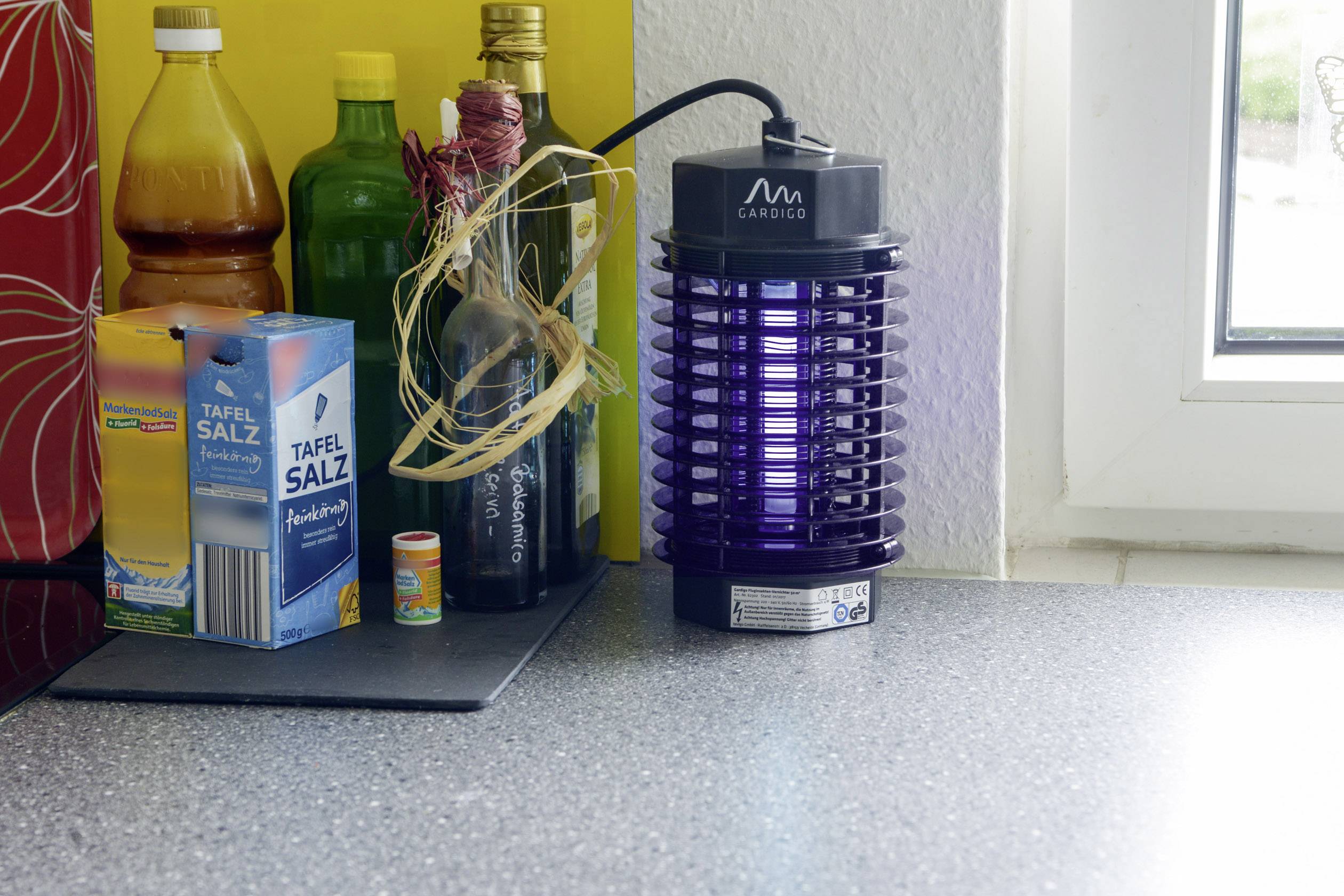 In een keuken staat een elektrische insectenval naast zout en flessen op een aanrecht.