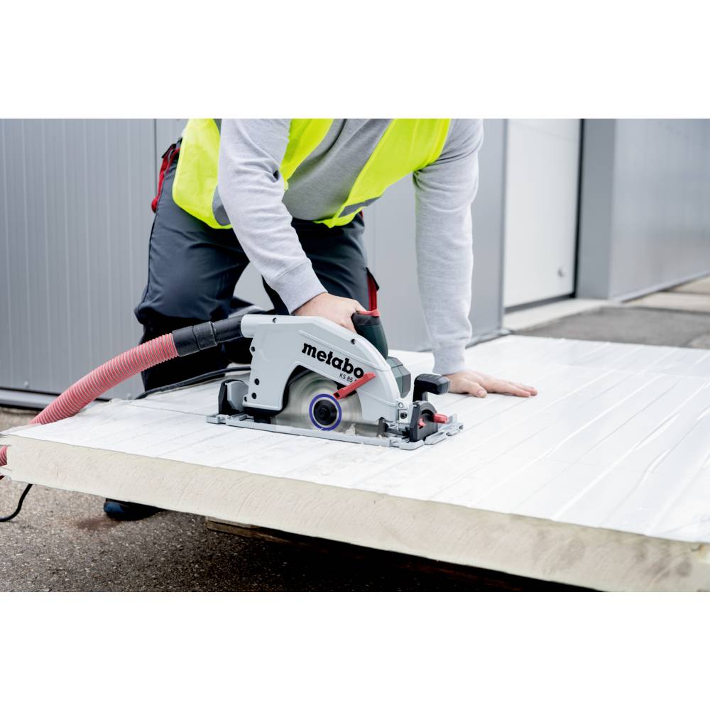 Een persoon in een veiligheidshesje gebruikt een cirkelzaag op een groot houten bord buiten, met de focus op constructiewerk.