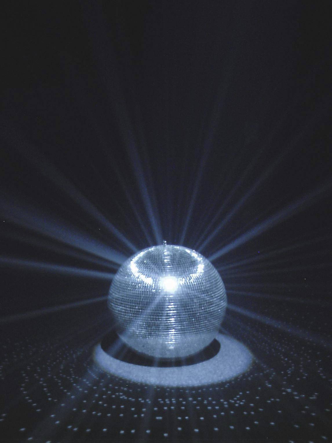 Een discobal weerkaatst lichtstralen in een donkere ruimte en creëert een patroon van lichtgevende punten op de vloer.