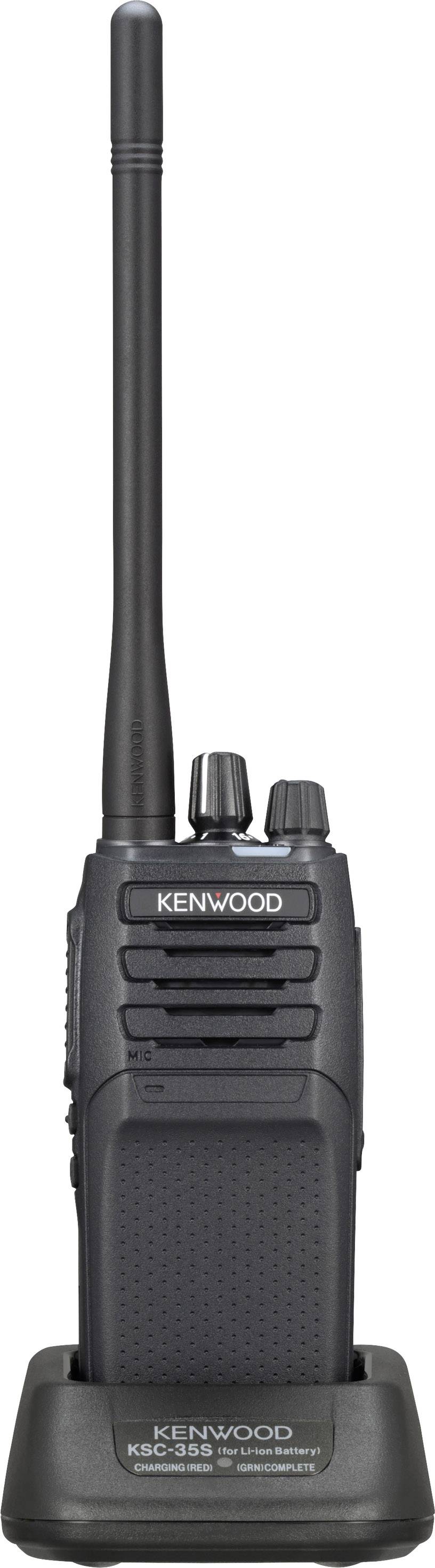 Een Kenwood-walkietalkie staat in een laadstation. Het heeft een lange antenne en verschillende knoppen voor bediening.