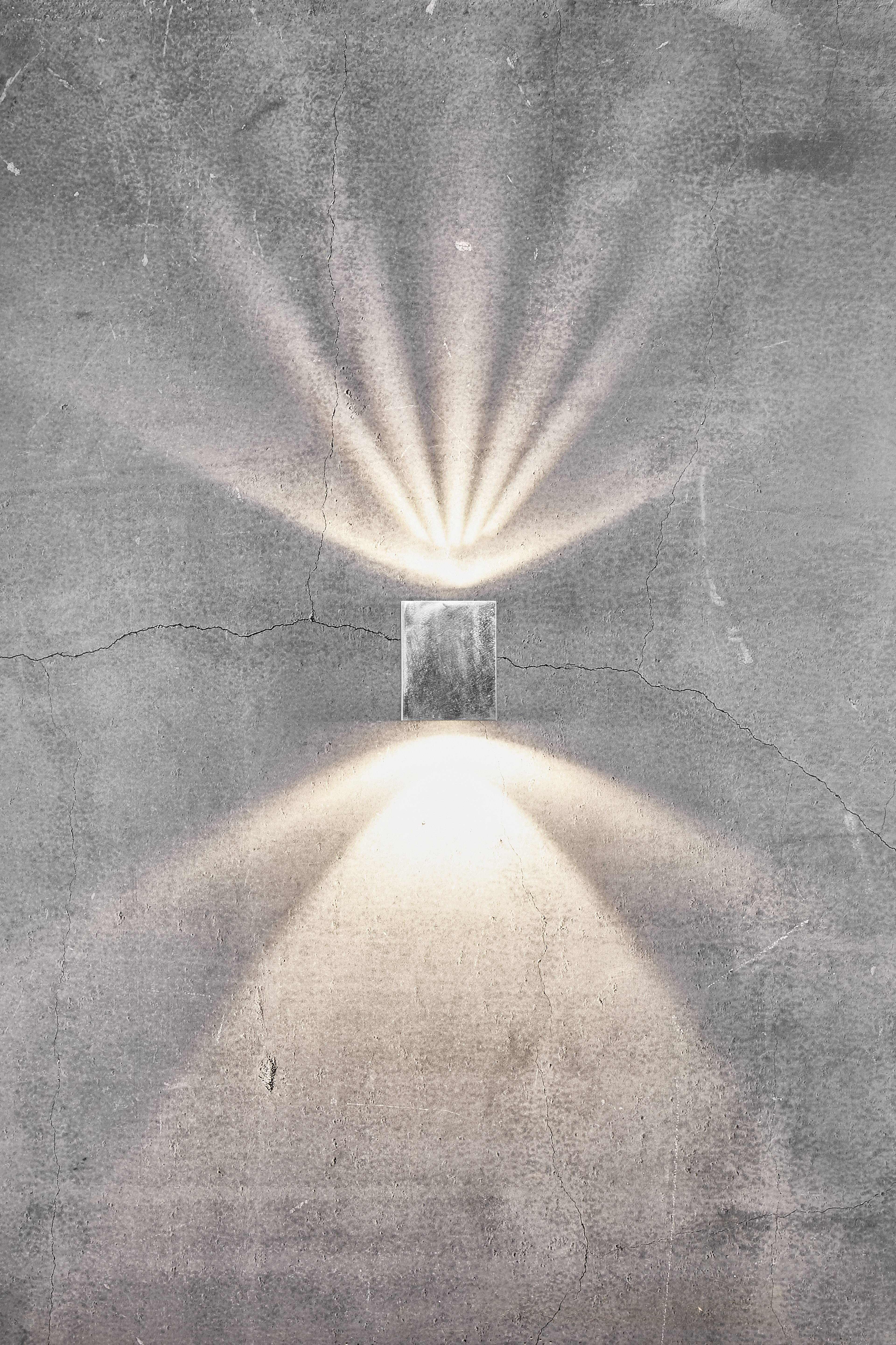 Een rechthoekig licht schijnt tegen een grijze muur en straalt heldere lichtbundels naar boven en beneden uit.