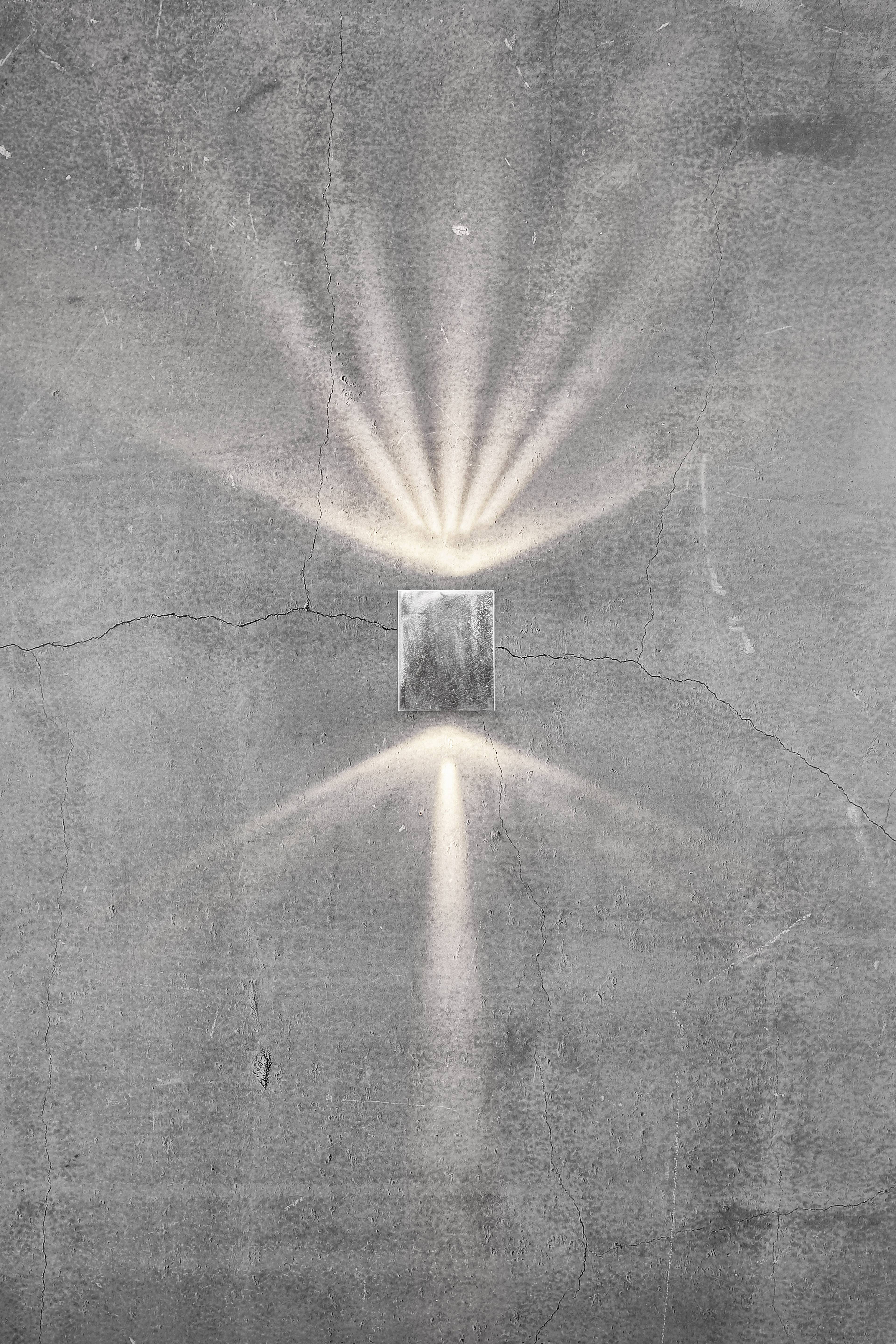 Een rechthoekig licht aan een grijze, gescheurde betonnen muur straalt heldere stralen in alle richtingen en creëert een patroon.