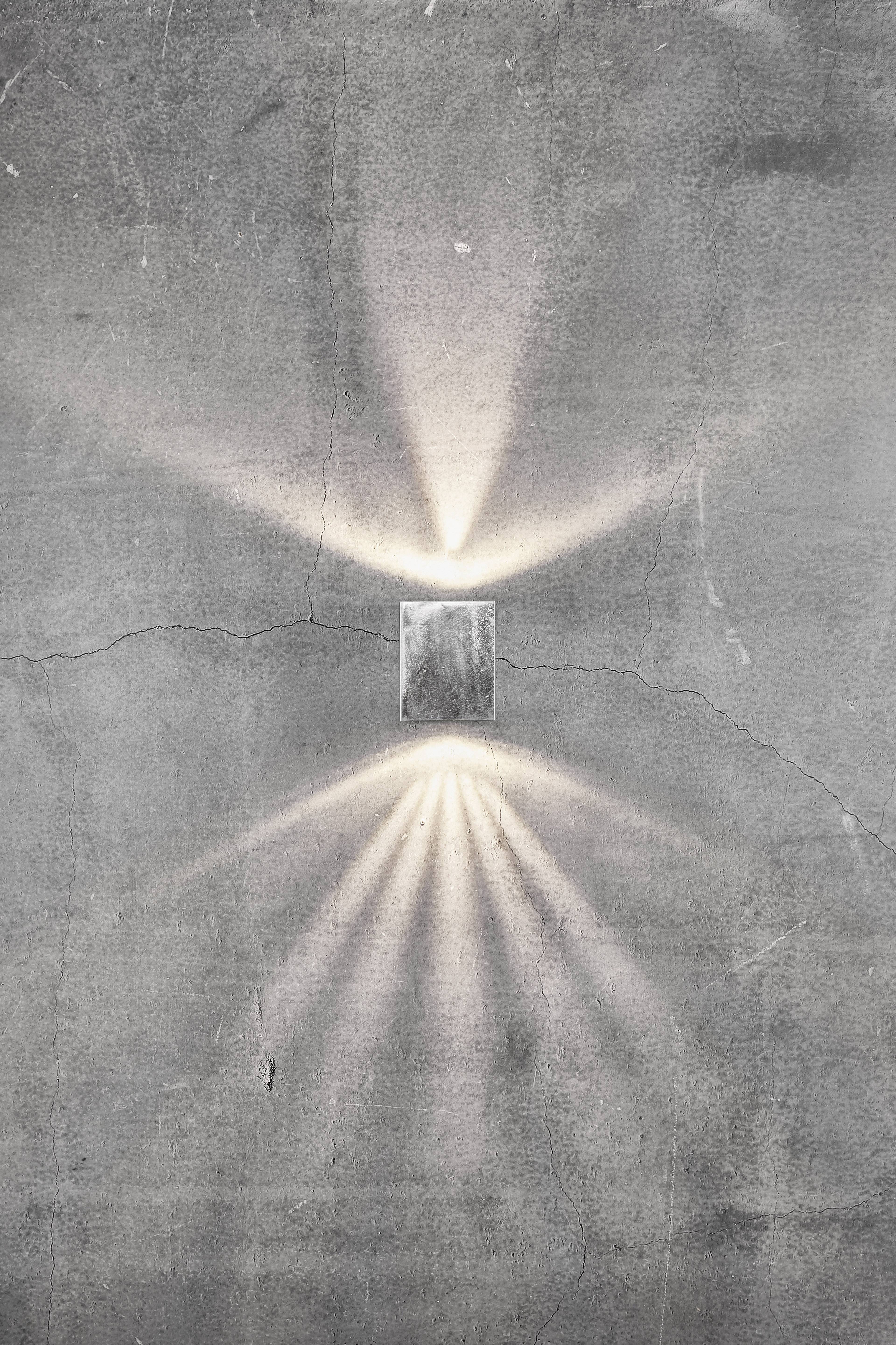Minimalistische wandtegel met moderne verlichtingseffect; lichtstralen worden gericht naar boven en beneden op ruwe betonnen muur.