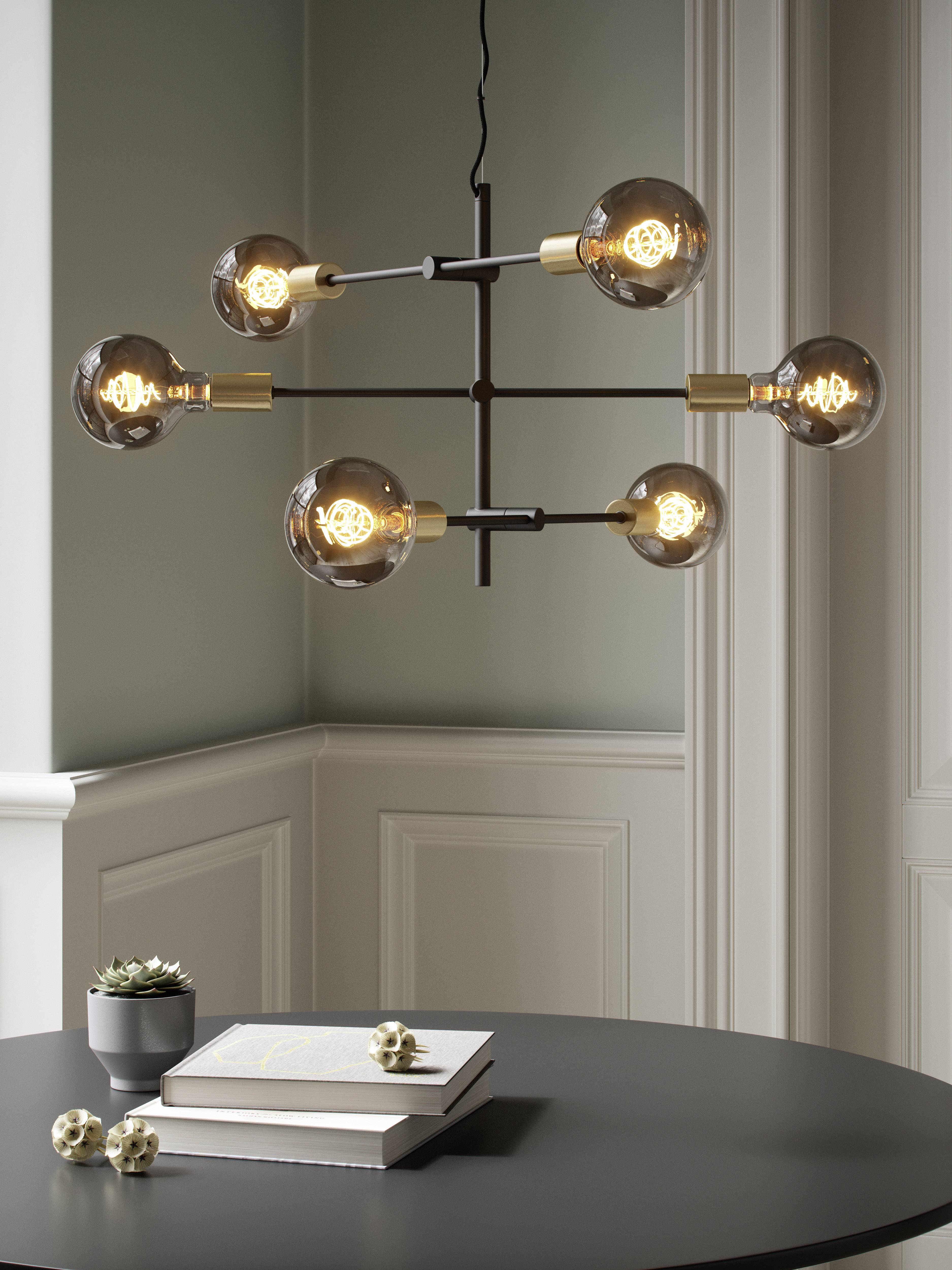Een moderne kroonluchter met zes gloeilampen hangt boven een ronde tafel, waarop boeken en een kleine plant staan.