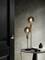 Staande lamp met twee lichtgevende gloeilampen op een kleine tafel naast een zwarte deur, minimalistisch interieur.
