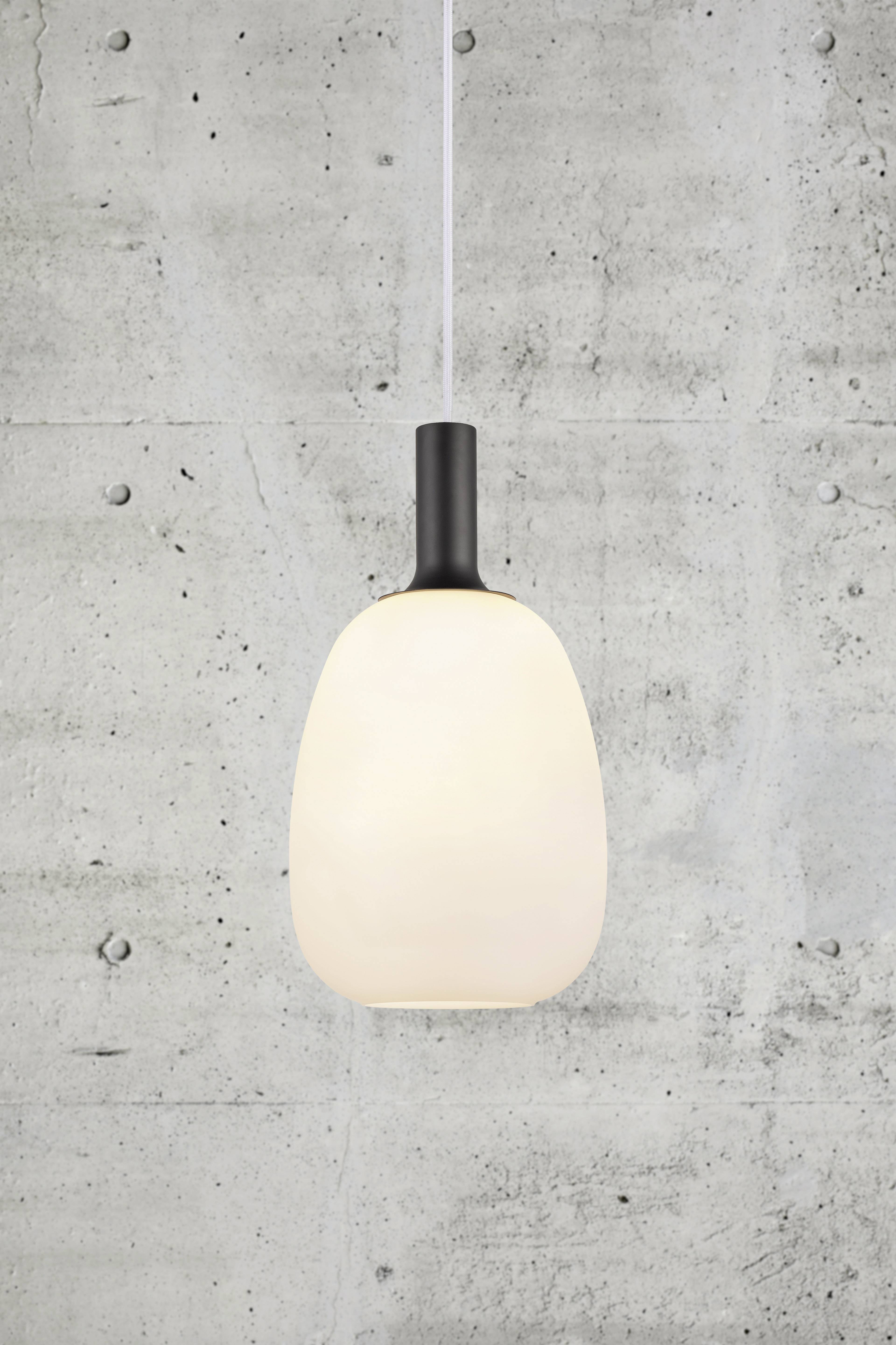 Witte, eivormige hanglamp voor een grijze betonnen muur, ingeschakeld en brandend.