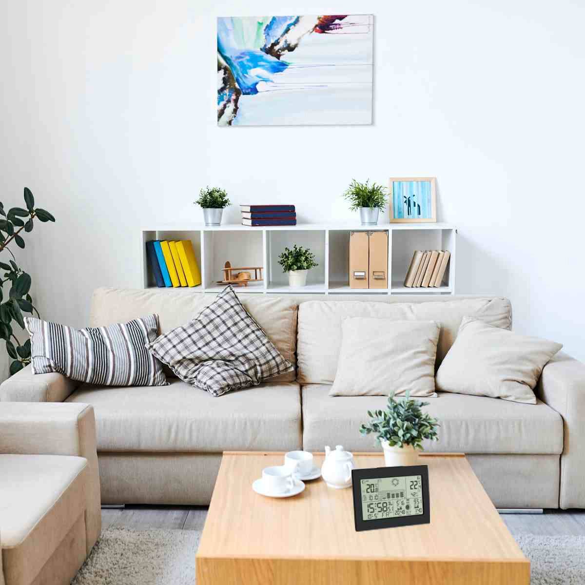 Lichte woonkamer met een lichtbruin bankstel, gestreepte kussens en een salontafel met kopjes. Wandplank met boeken en planten, abstract schilderij aan de muur.