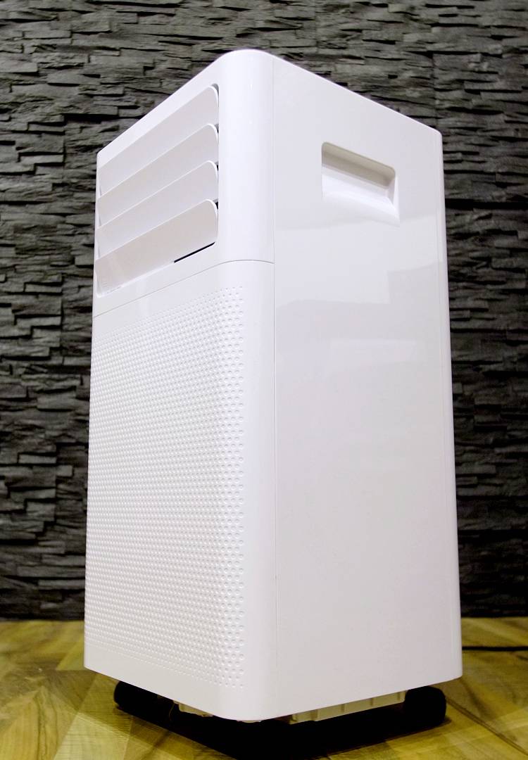 Een witte luchtreiniger staat op een houten vloer voor een donkere, gestructureerde muur.