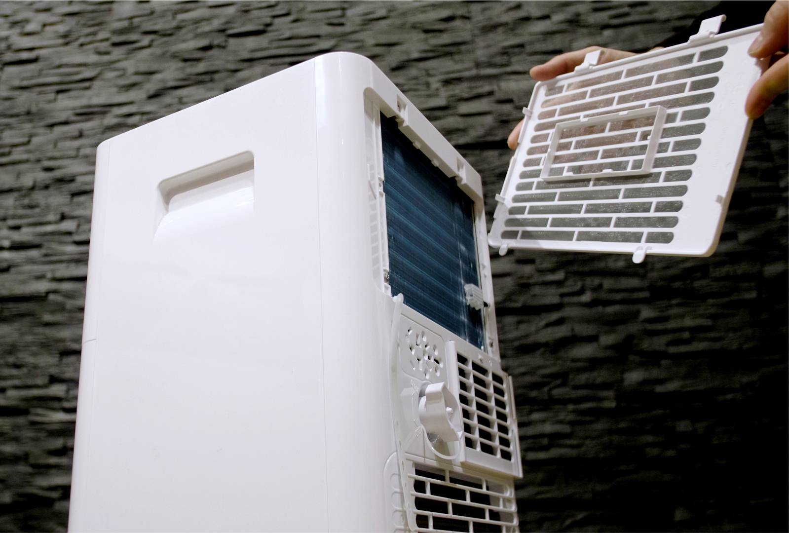 Een persoon opent de afdekking van een draagbare luchtreiniger om het filter te vervangen of schoon te maken.