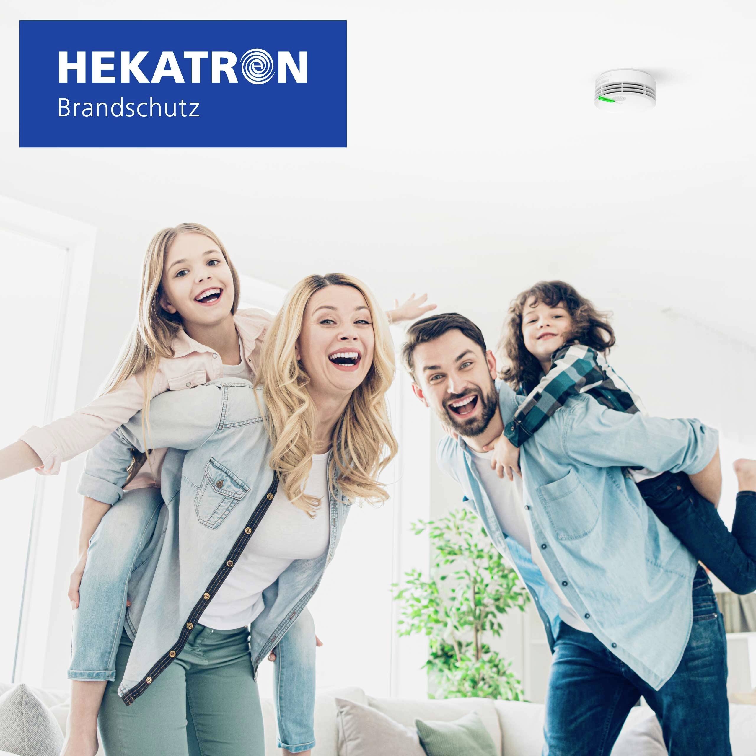 Een gezin van vier lacht en poseert vrolijk in een helder verlichte ruimte. Het Hekatron Brandschutz-logo is zichtbaar in de linkerbovenhoek.