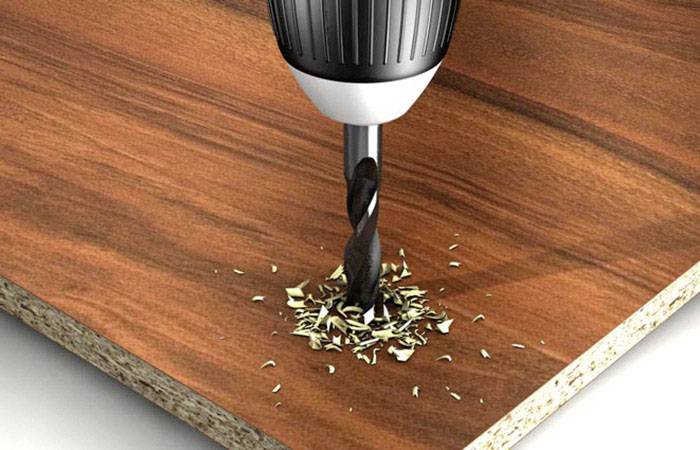 Een zwarte boor boort een gat in een houten plaat, omringd door kleine houtspaanders.