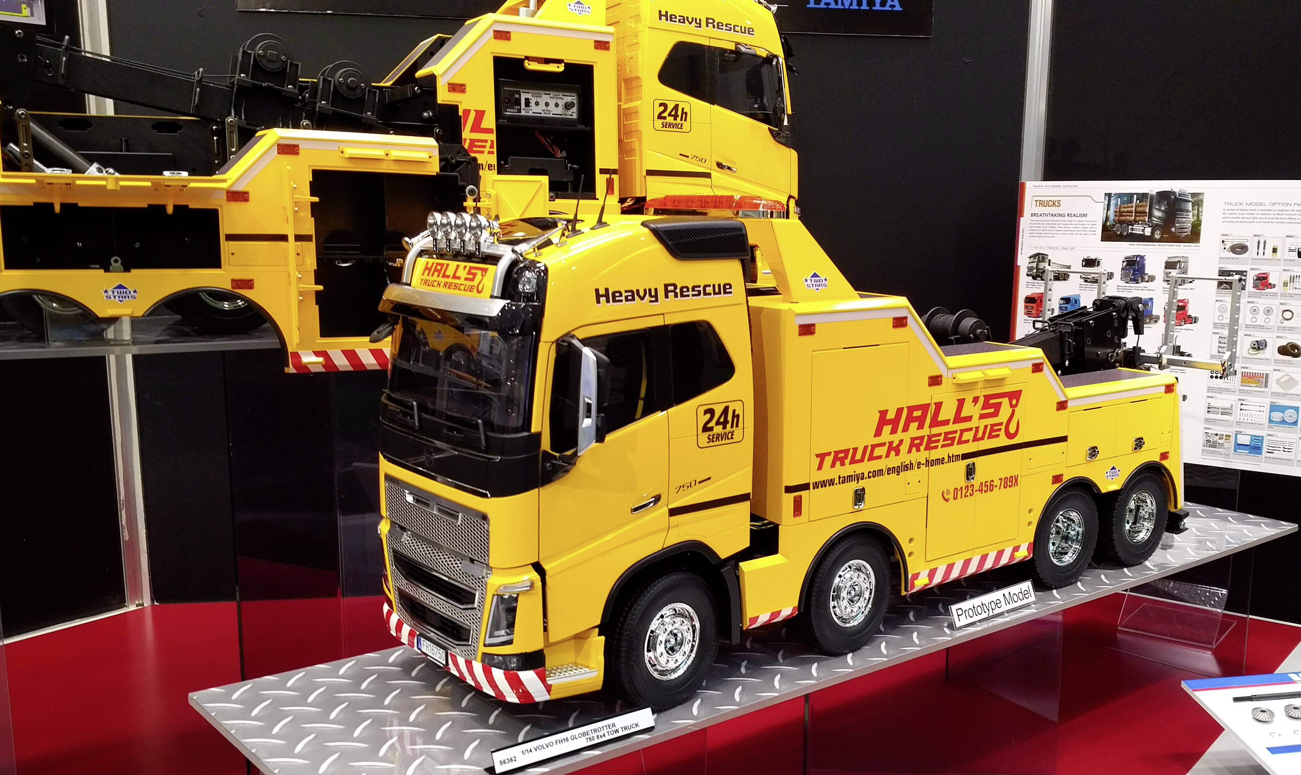Een geel model van een bergingsvoertuig met 'Hall's Truck Rescue' opschrift staat op een tentoonstellingsstand, omringd door informatieposters.