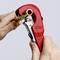 Een hand gebruikt een rood buizensnijgereedschap om een pijp door te snijden. Op het gereedschap is de merknaam "Knipex" zichtbaar.