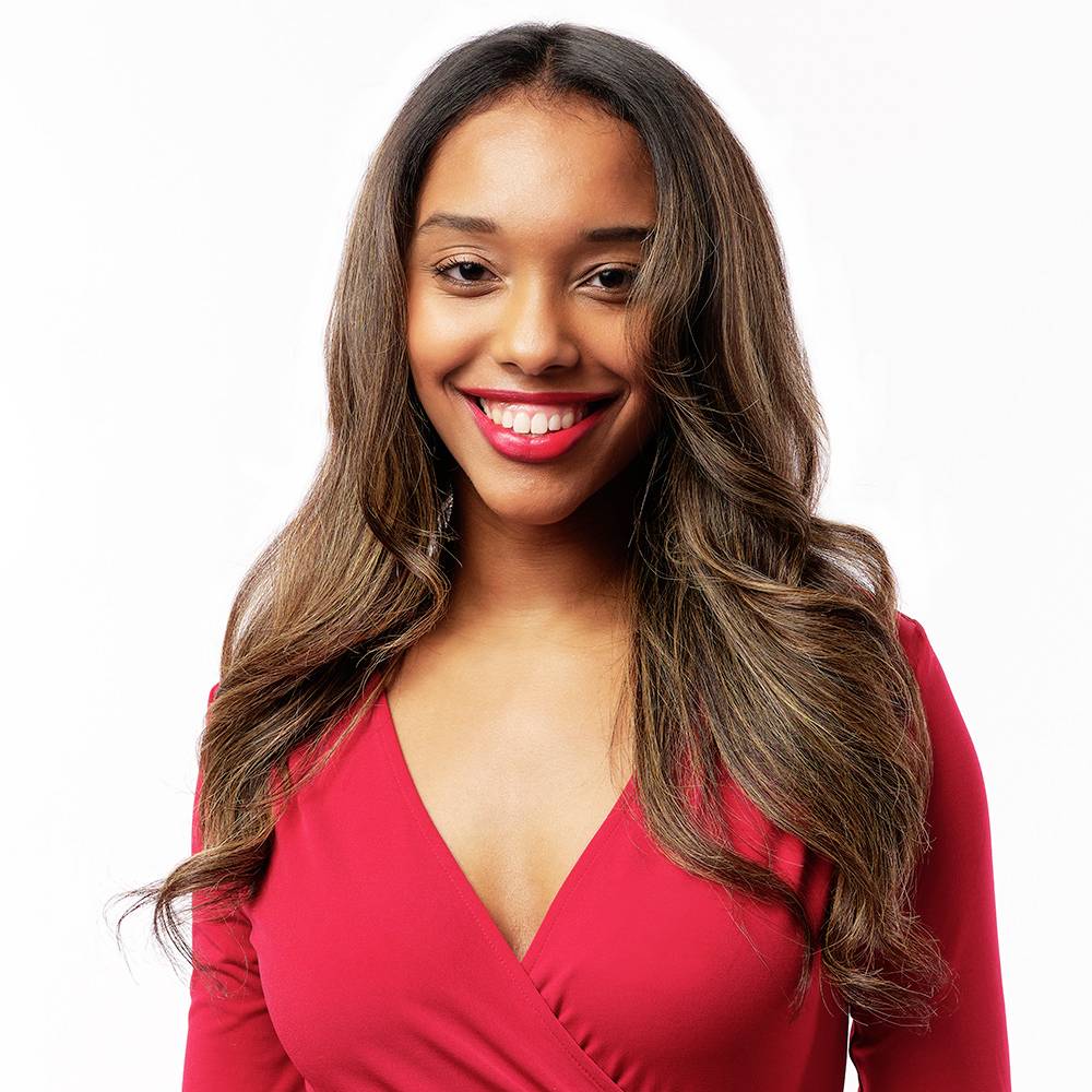 Een lachende persoon met lang bruin haar draagt een rood bovenkleding.