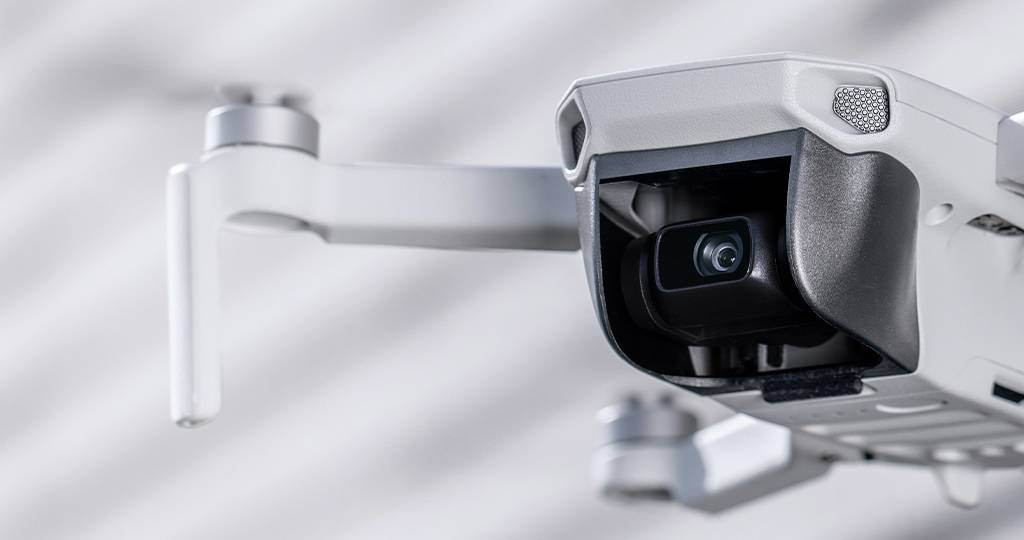 Close-up van een witte drone met camera, gericht naar de kijker. De achtergrond is onscherp.