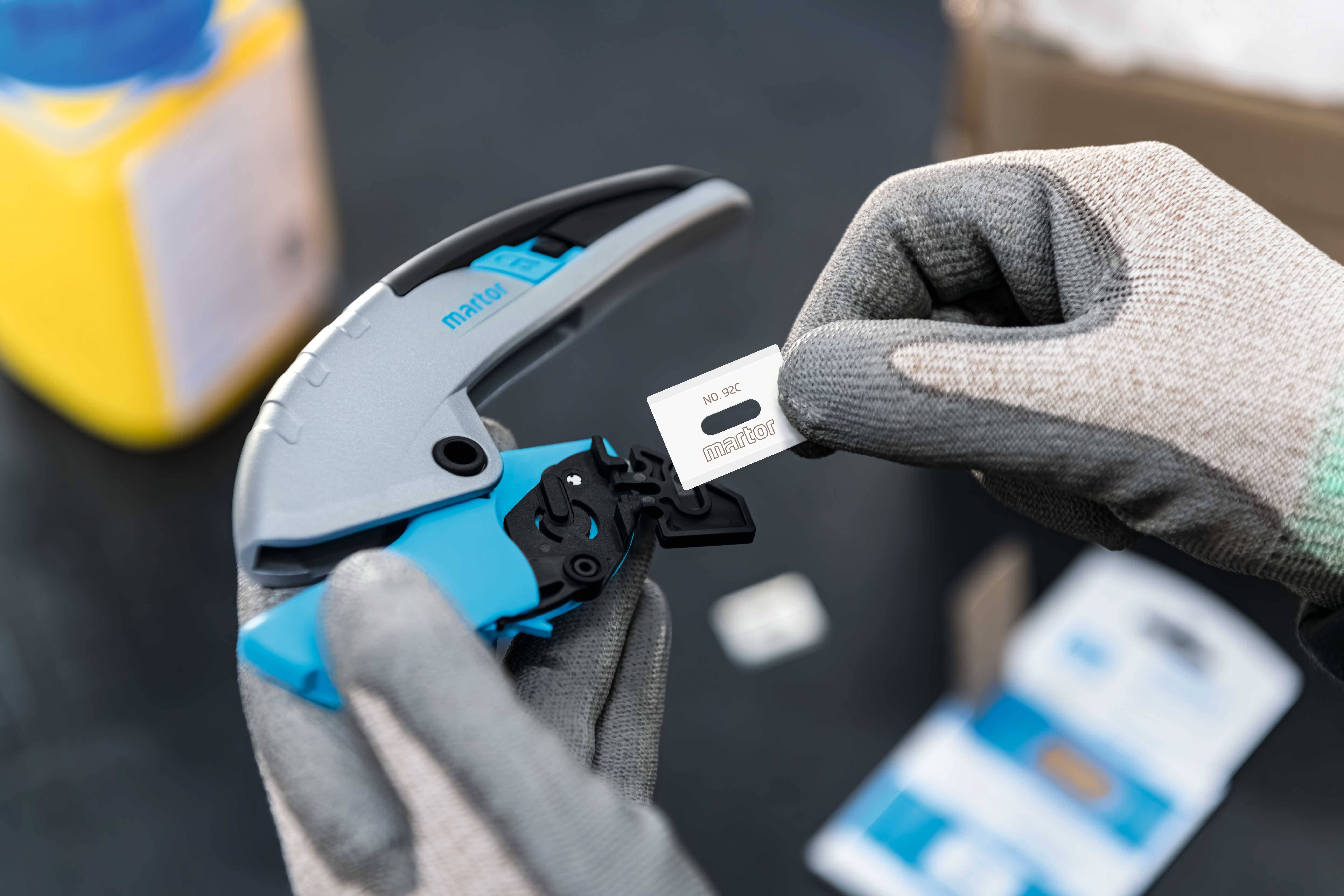 Een persoon draagt handschoenen en houdt een gereedschap vast in de linkerhand. In de rechterhand wordt een etiket vastgehouden met de tekst 'NO.16'.