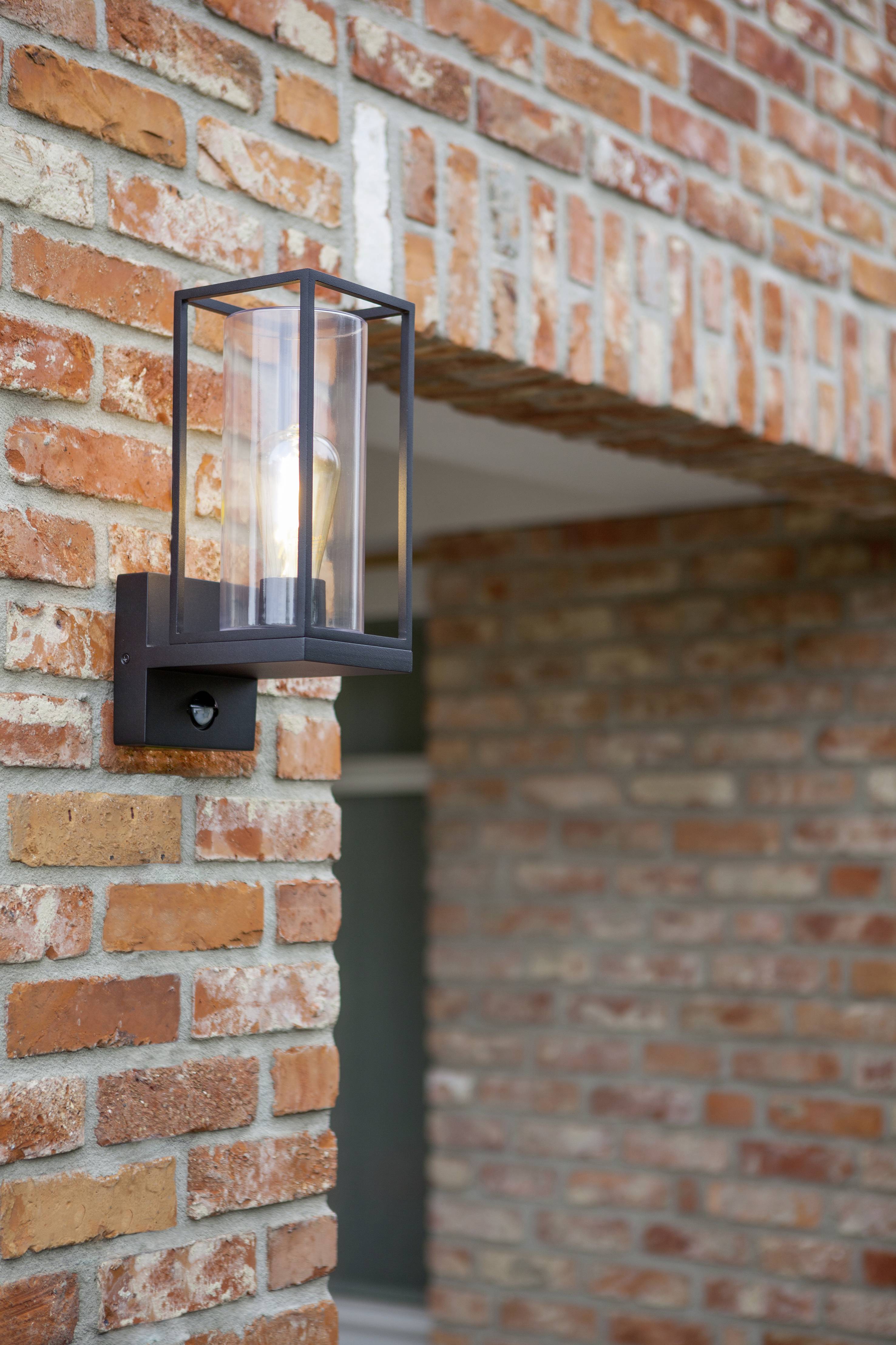 Een moderne wandlamp met een glazen behuizing, gemonteerd aan een rode bakstenen muur, verlicht zwak het gebied eronder.