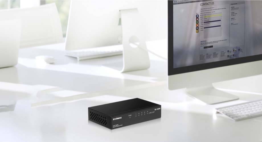 Een zwarte netwerk-switch staat op een modern bureau, omringd door computermonitors en andere kantoorbenodigdheden.