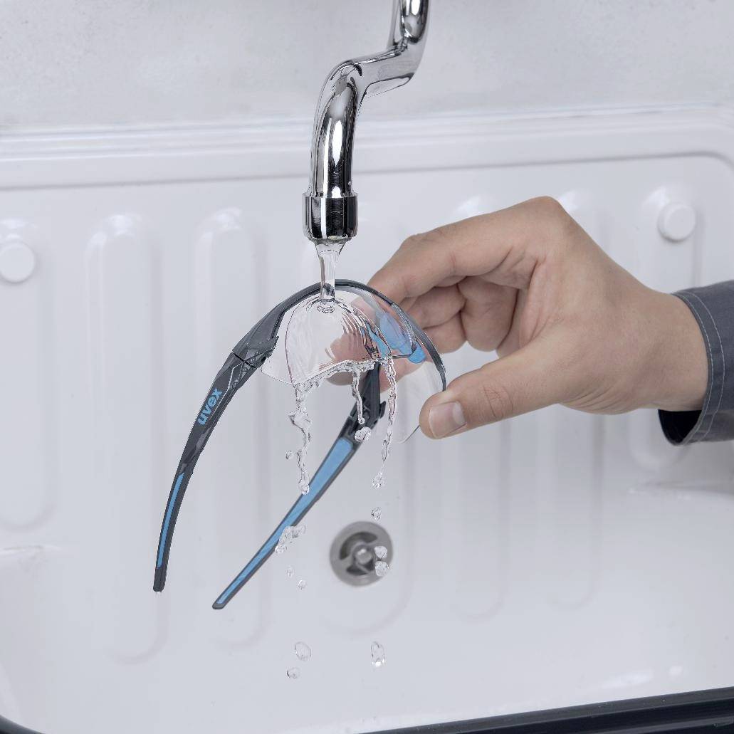 Een hand reinigt een haarverzorgingsapparaat onder stromend water in een wasbak.
