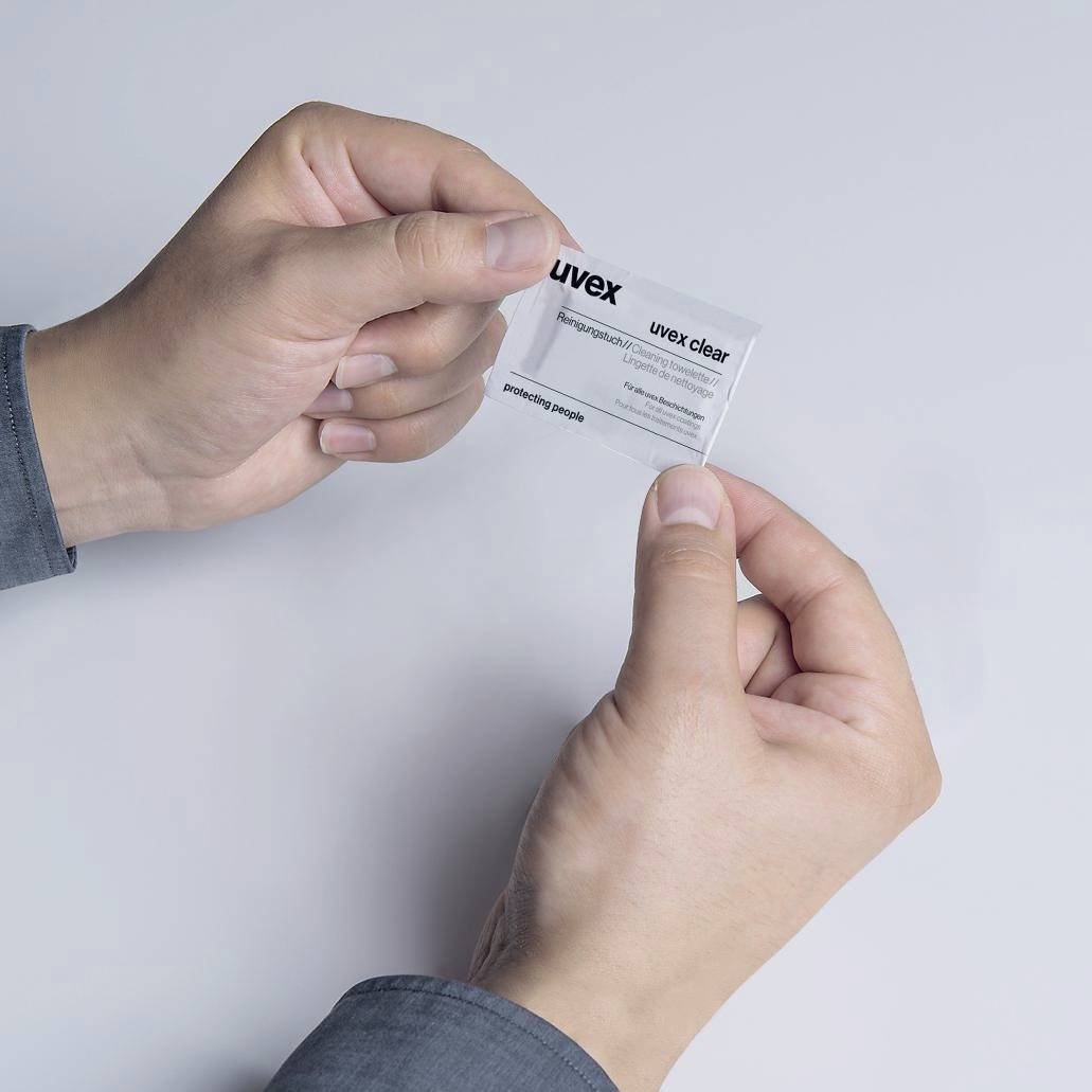 Een persoon houdt een Uvex-verpakking met reinigingsdoekjes in de hand. De doekjes zijn bedoeld voor het reinigen van veiligheidsbrillen.