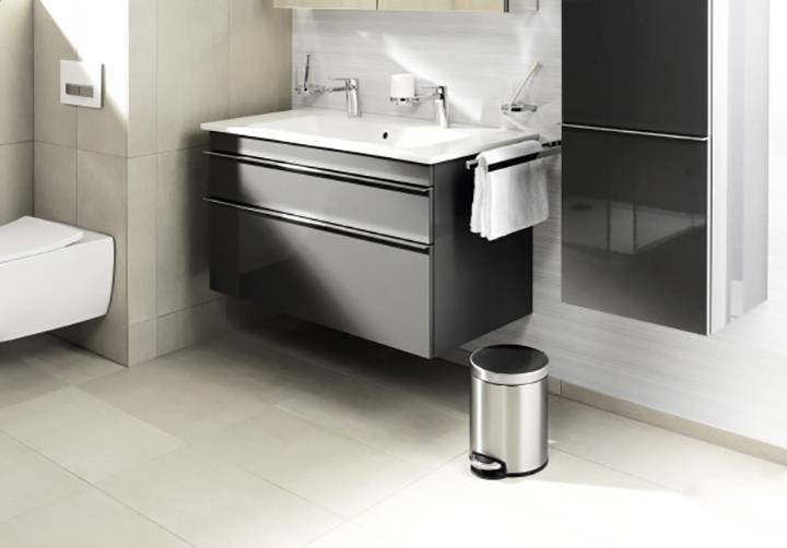 Modern badkamer met een laag hangend zwart wastafelmeubel, ruim wastafelblad, chromen kranen en prullenbak.